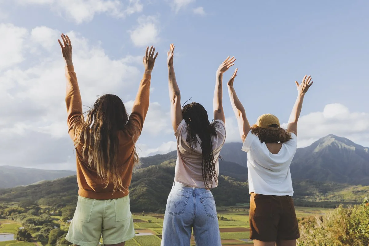 Three people with raised arms standing in front of a scenic mountain landscape.