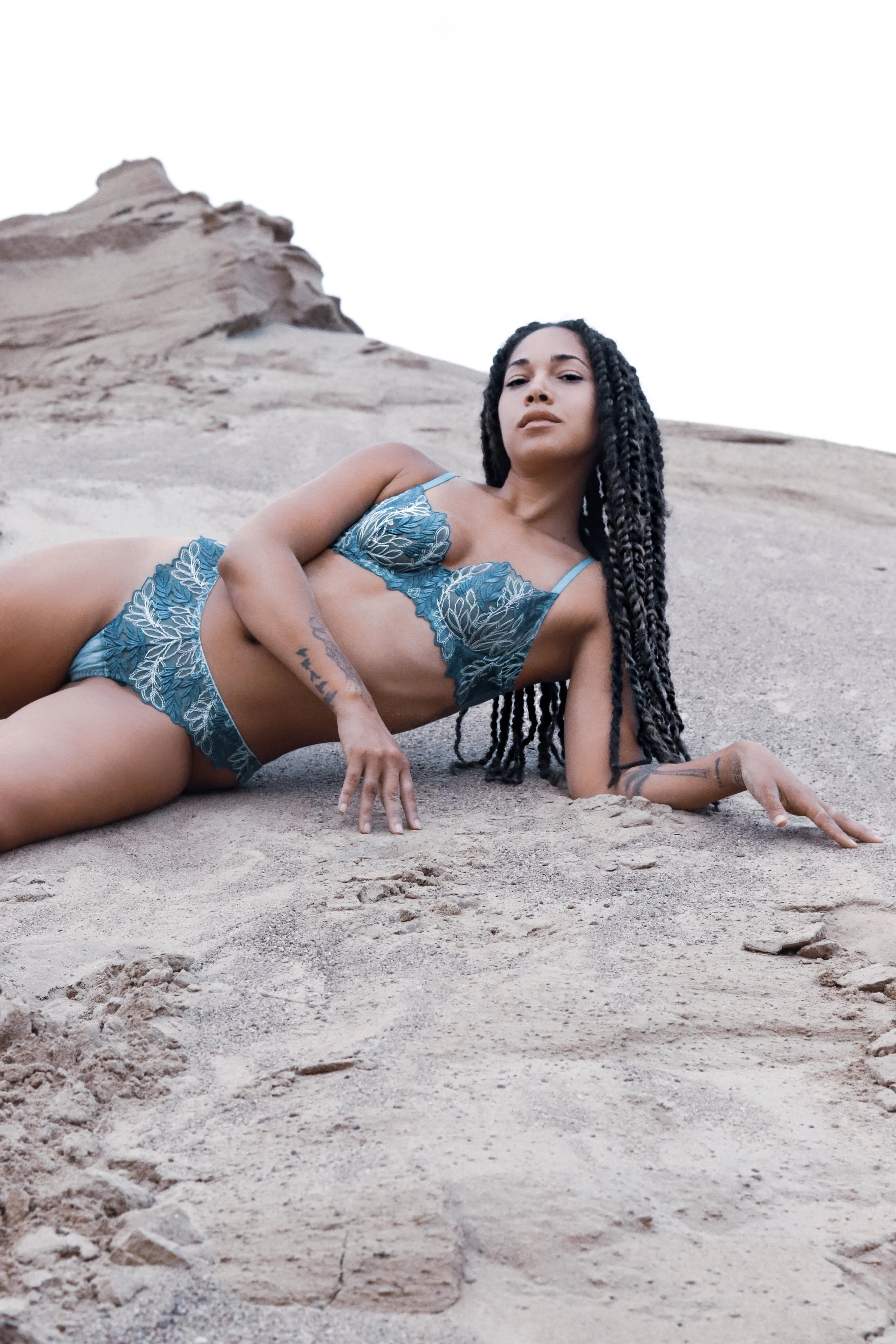 Person posing on a sandy terrain wearing blue lace lingerie.