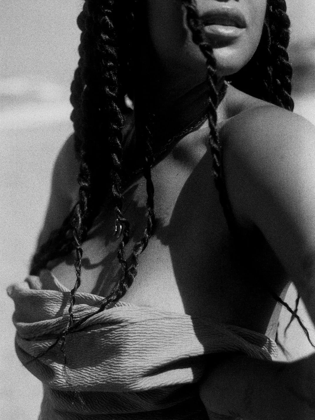 Black and white close-up of a person with braided hair and an off-shoulder top.