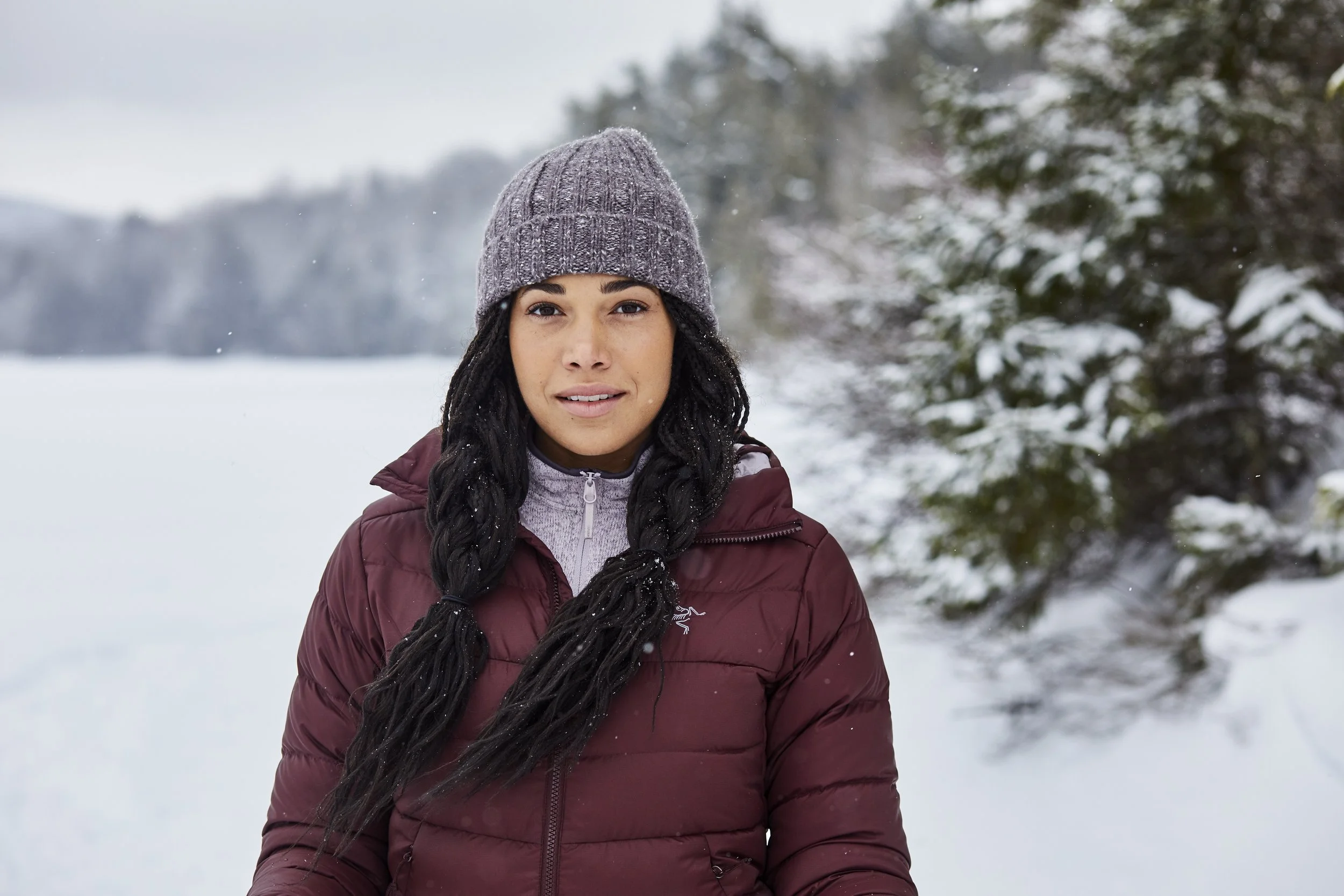 Person wearing a maroon jacket and gray knit hat in a snowy outdoor setting.