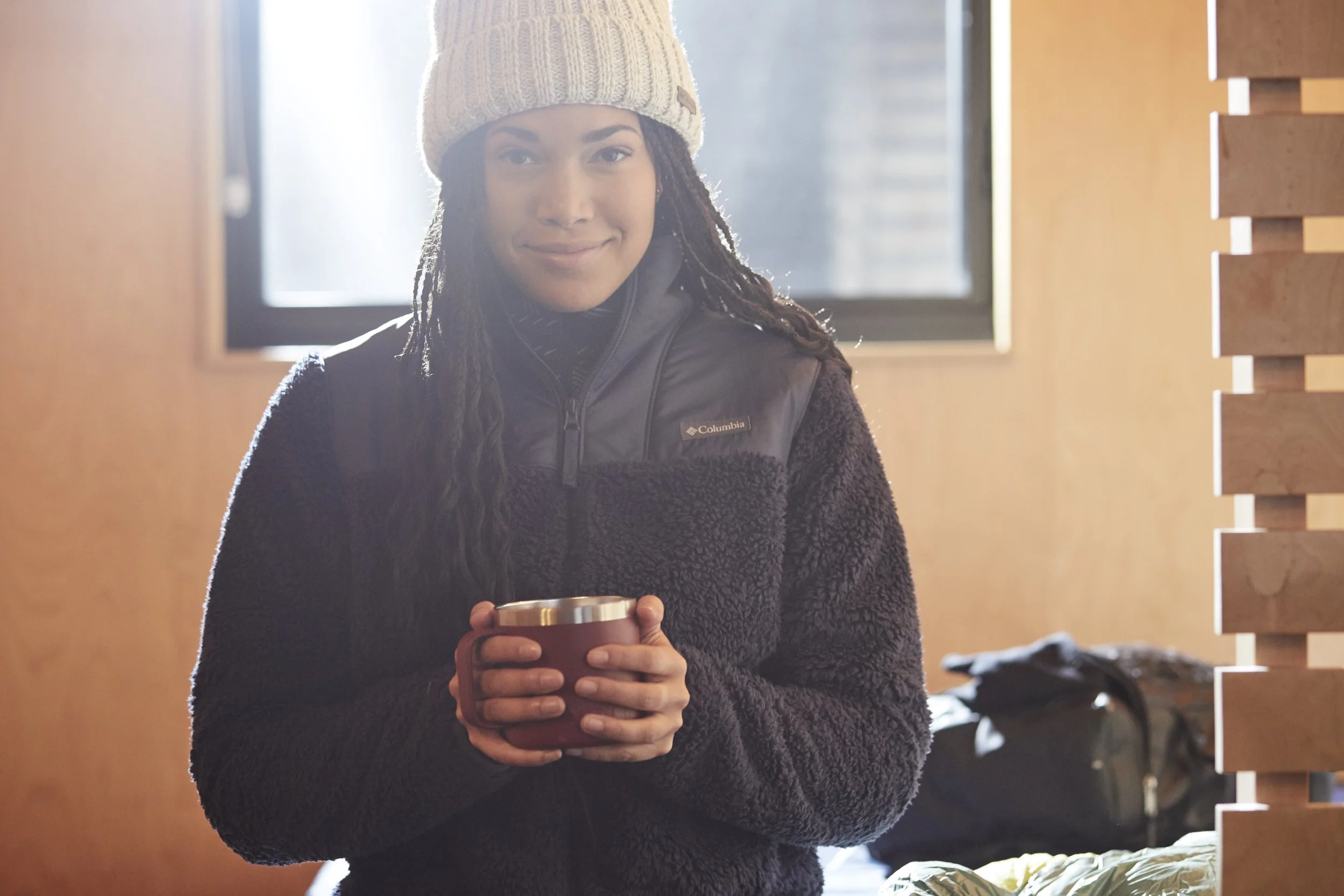 Person wearing winter clothing holding a mug indoors.