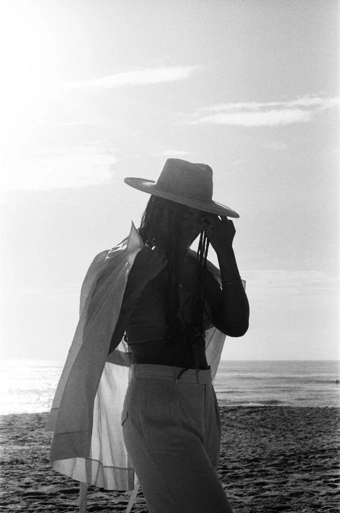 Silhouette of a person wearing a hat and jacket at the beach, with the ocean and sky in the background.