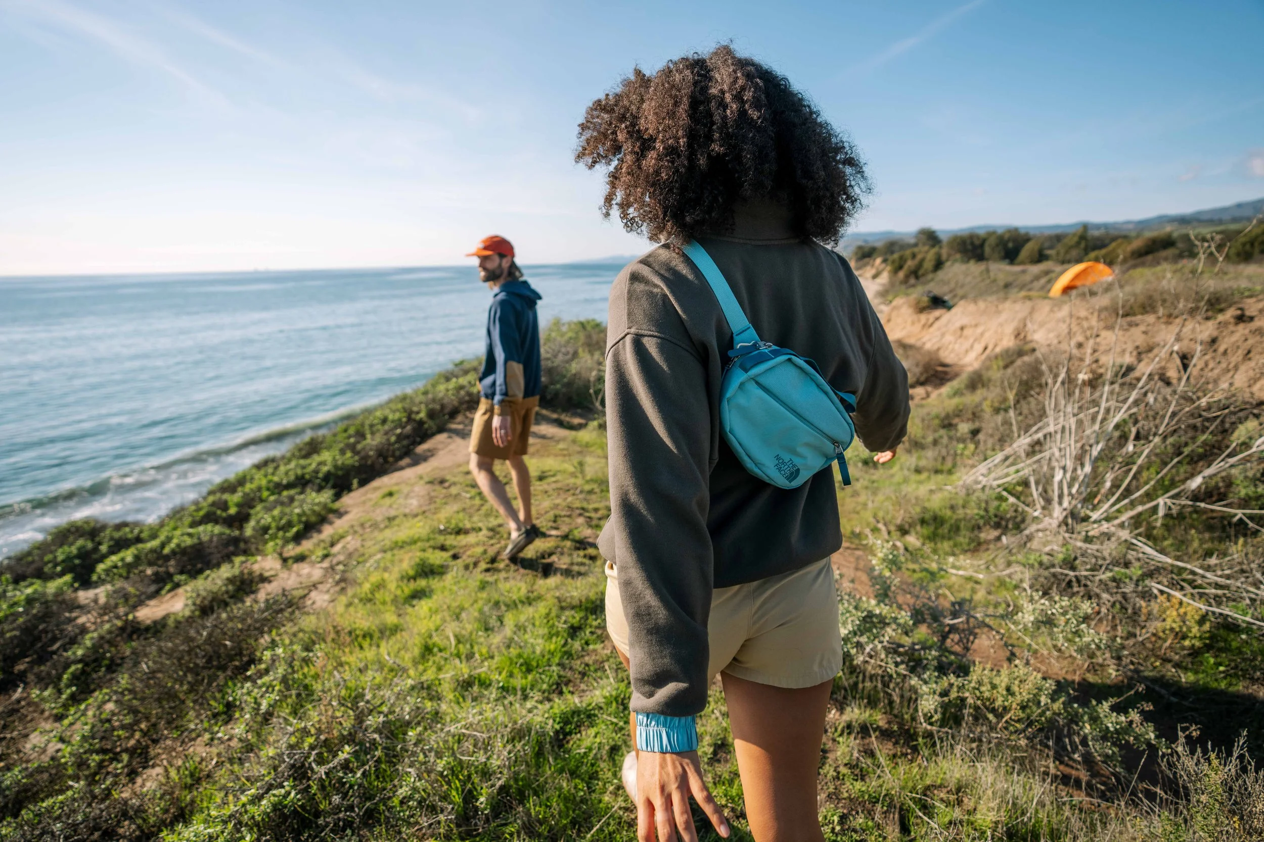 Two people walking on a grassy coastal trail overlooking the ocean.