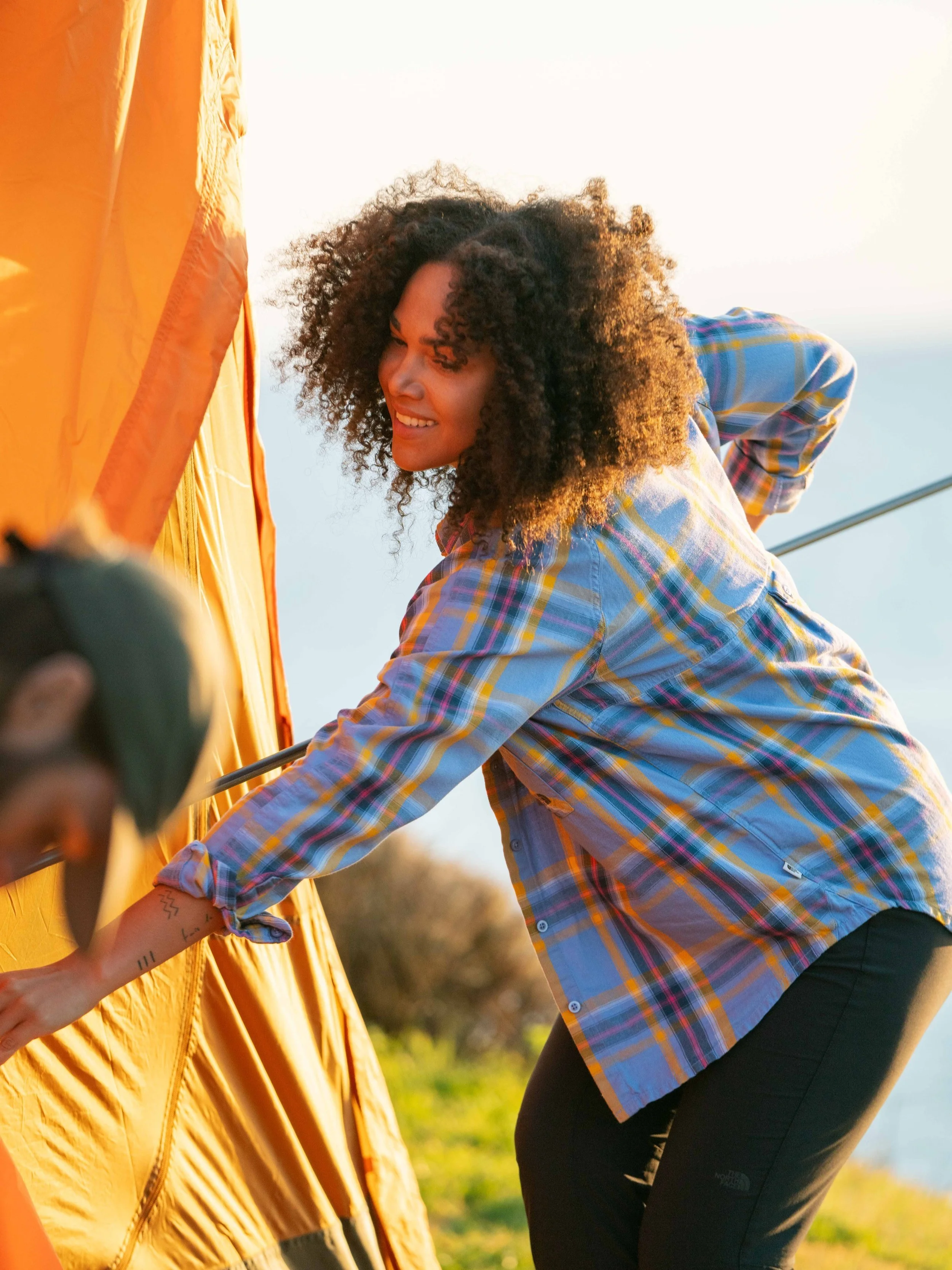 Person setting up an orange tent outdoors during daylight.