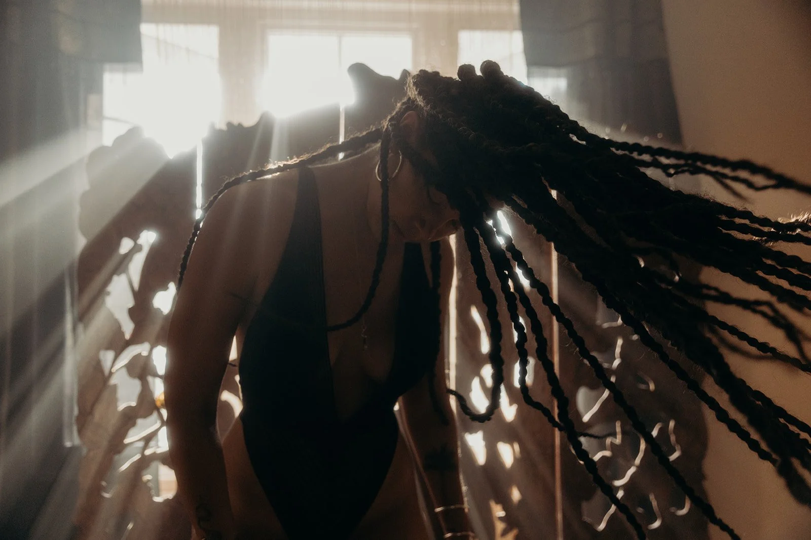 Person with long braids casting head down, sunlight streaming through window in background