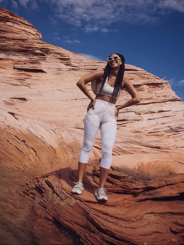 Person in white athletic wear posing on a red rock formation under a blue sky.