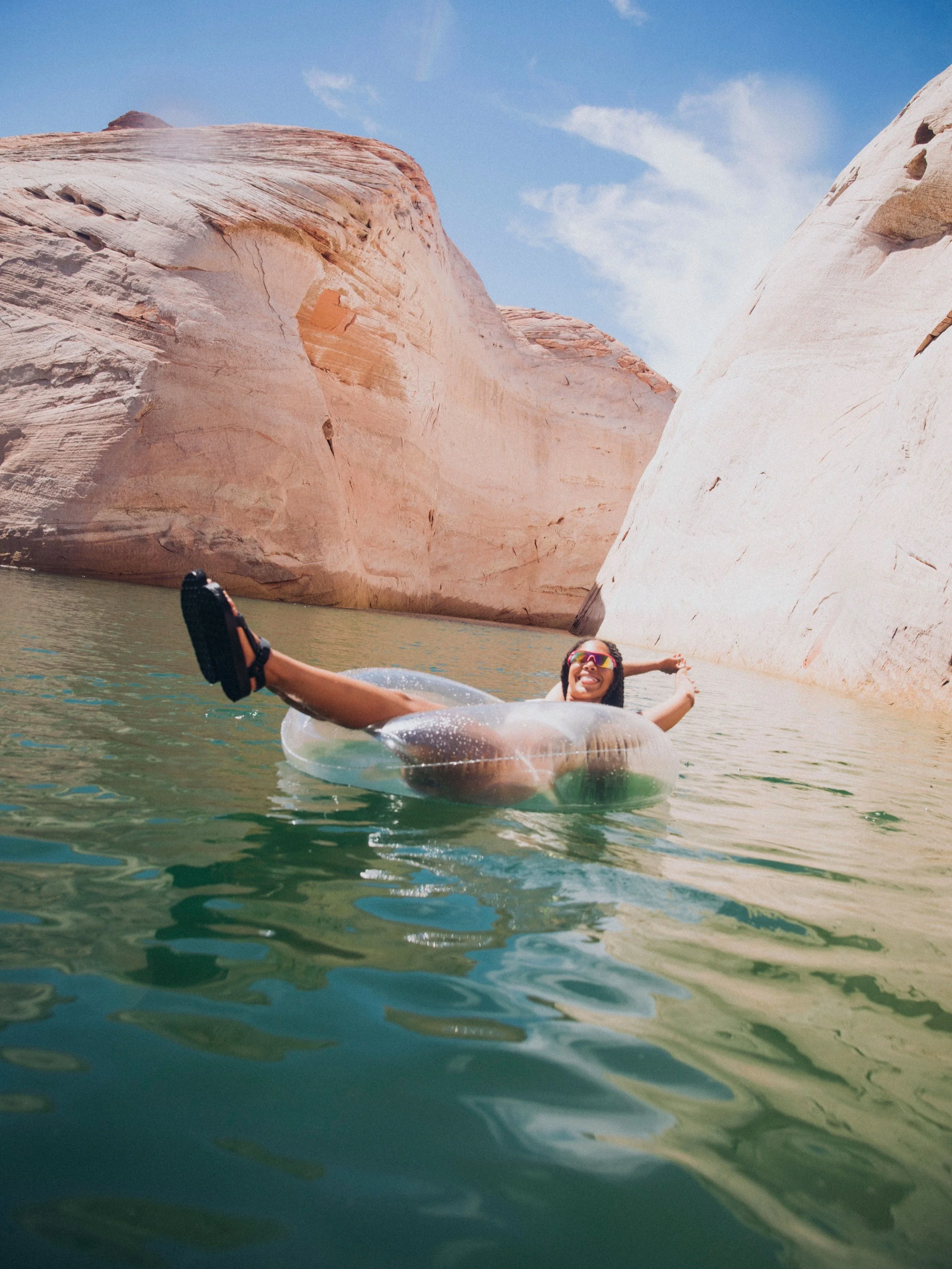 Person relaxing in an inflatable tube on a calm lake surrounded by canyons.
