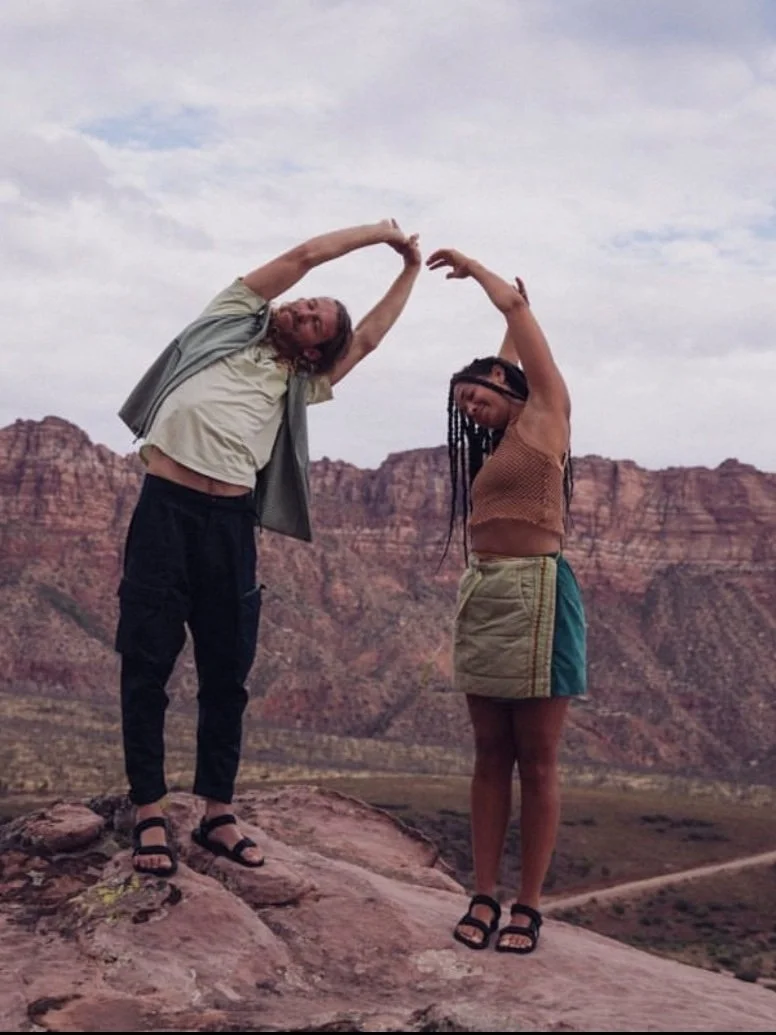 Two people doing yoga poses on a rocky landscape with a desert backdrop.