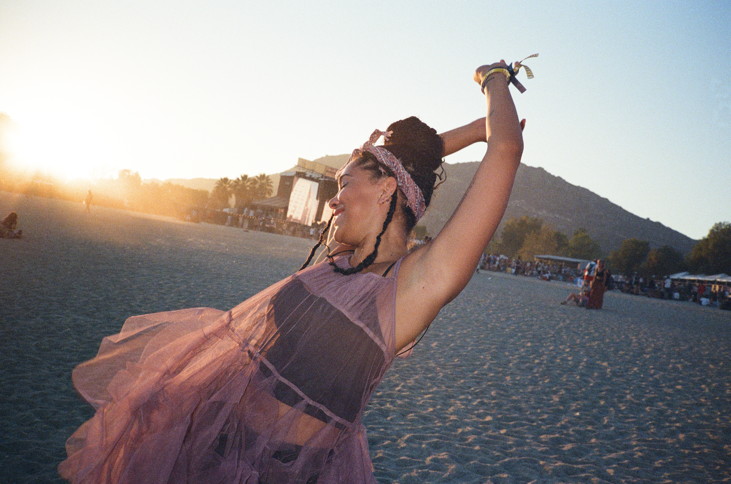 Woman dancing on a sandy beach at sunset with a mountain in the background.
