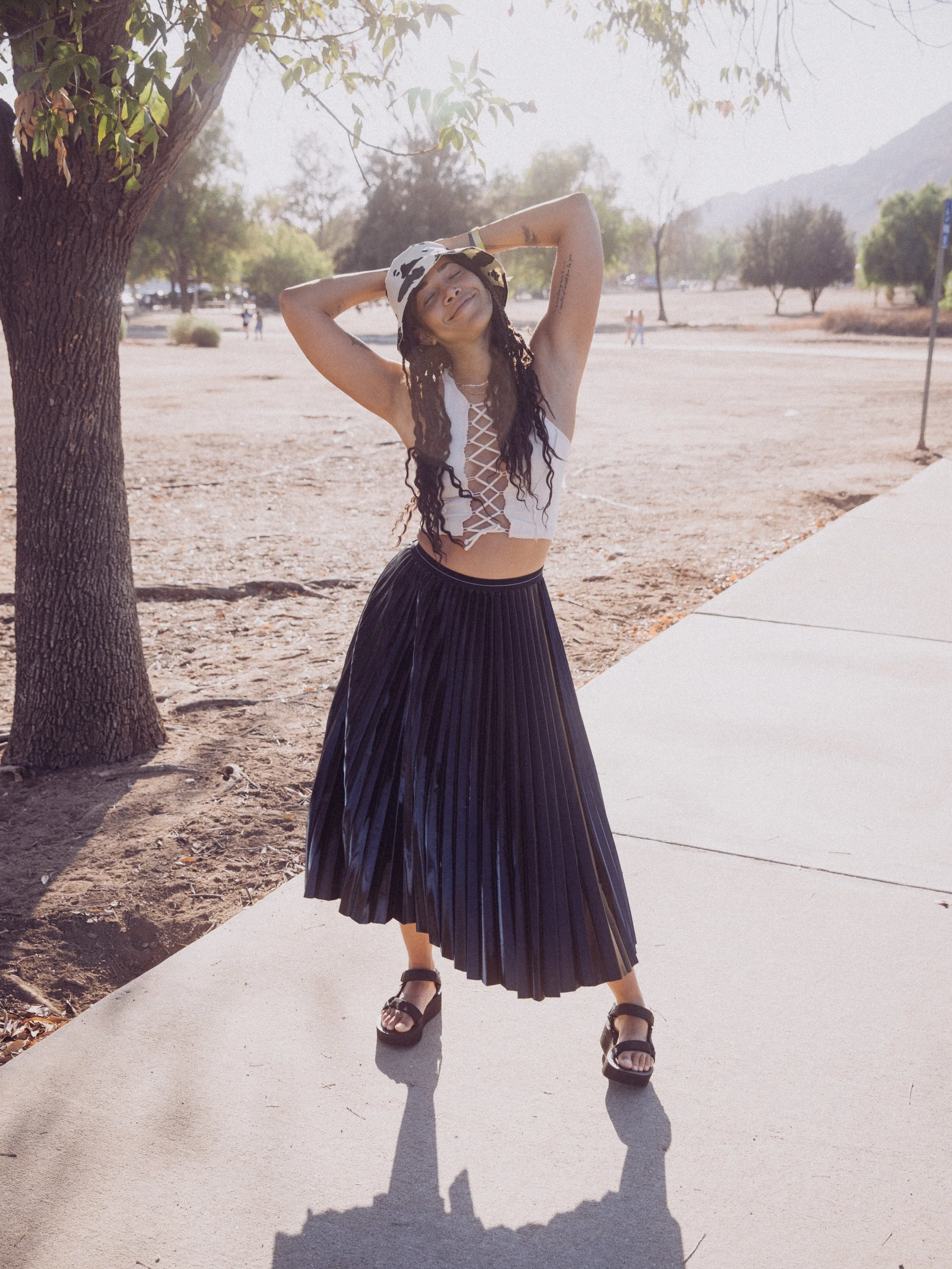 Woman wearing a white top and black skirt, posing outdoors in sunlight.
