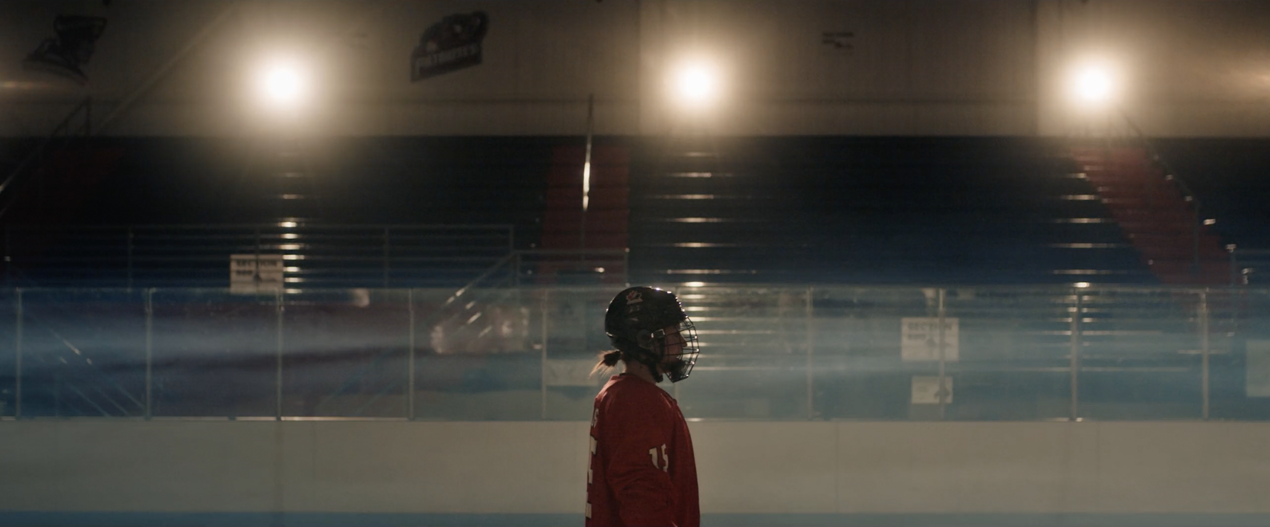 Hockey player wearing red jersey and black helmet stands on an ice rink.