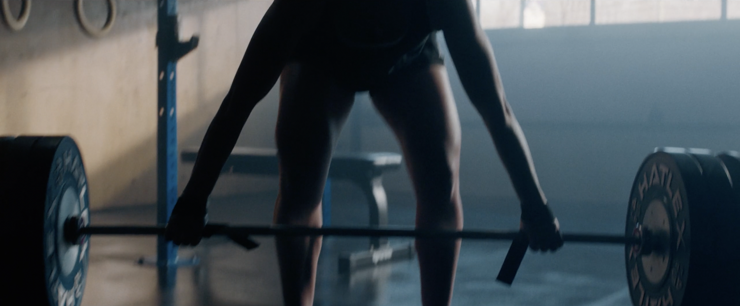 Person lifting a heavy barbell in a gym with workout equipment.