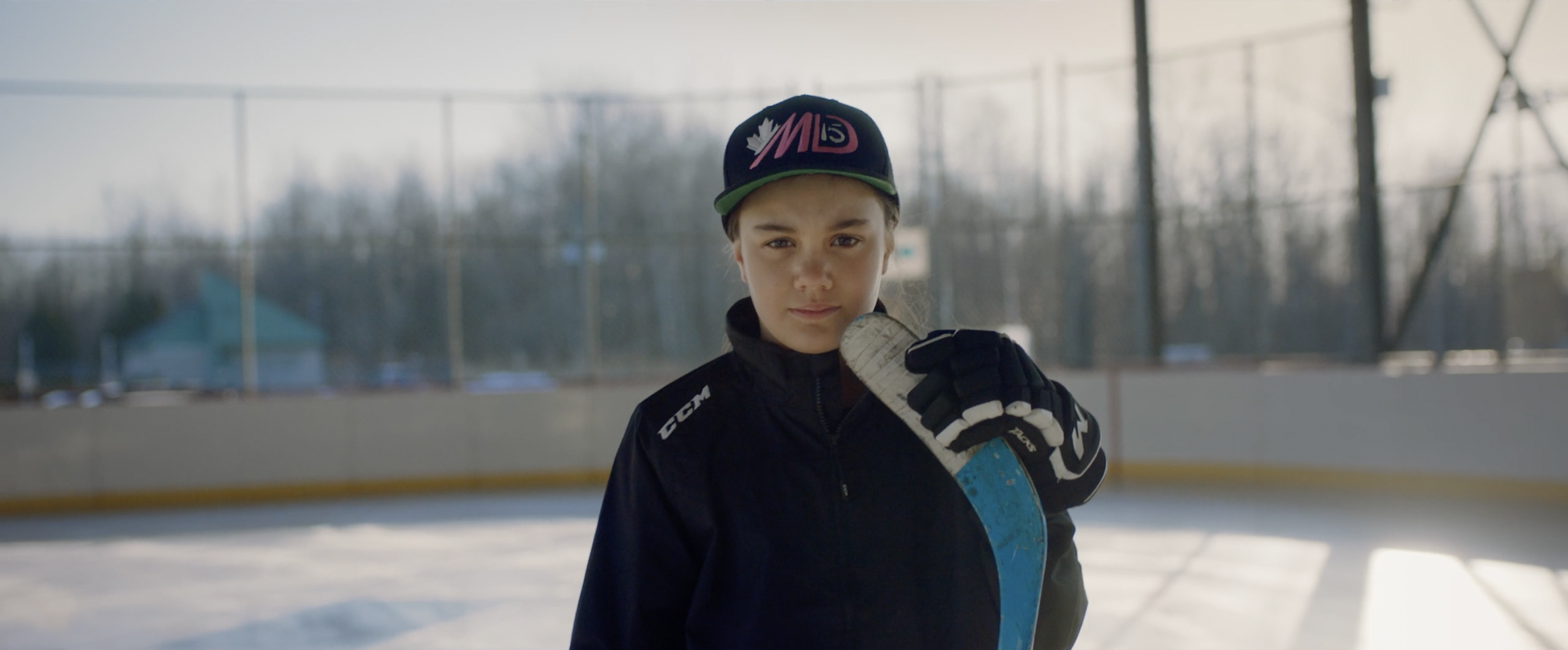 Young hockey player with hat and gloves holding a hockey stick on an outdoor rink.