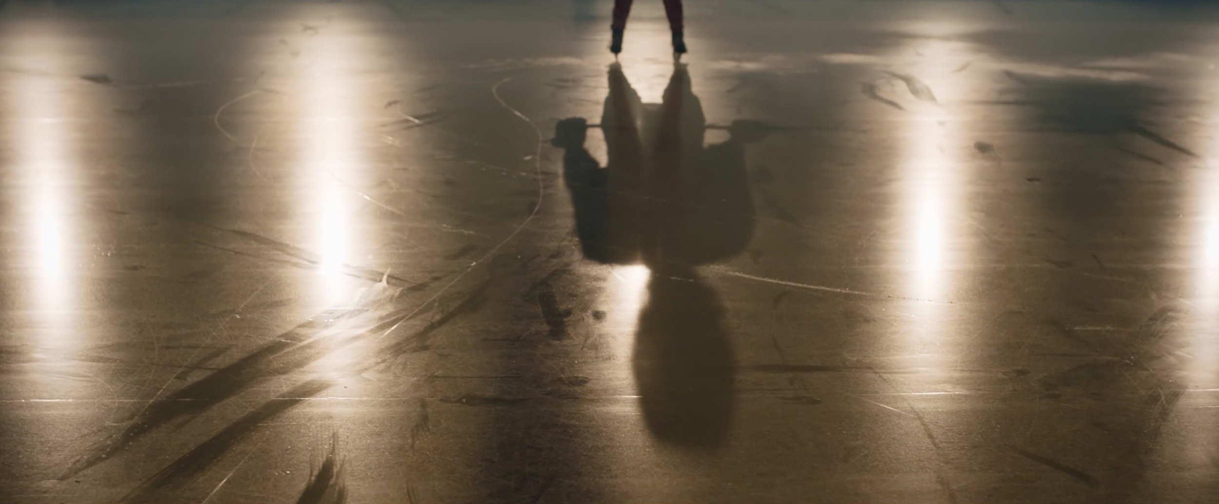 Shadow of a person skating on a polished ice surface with visible skate marks and reflections.