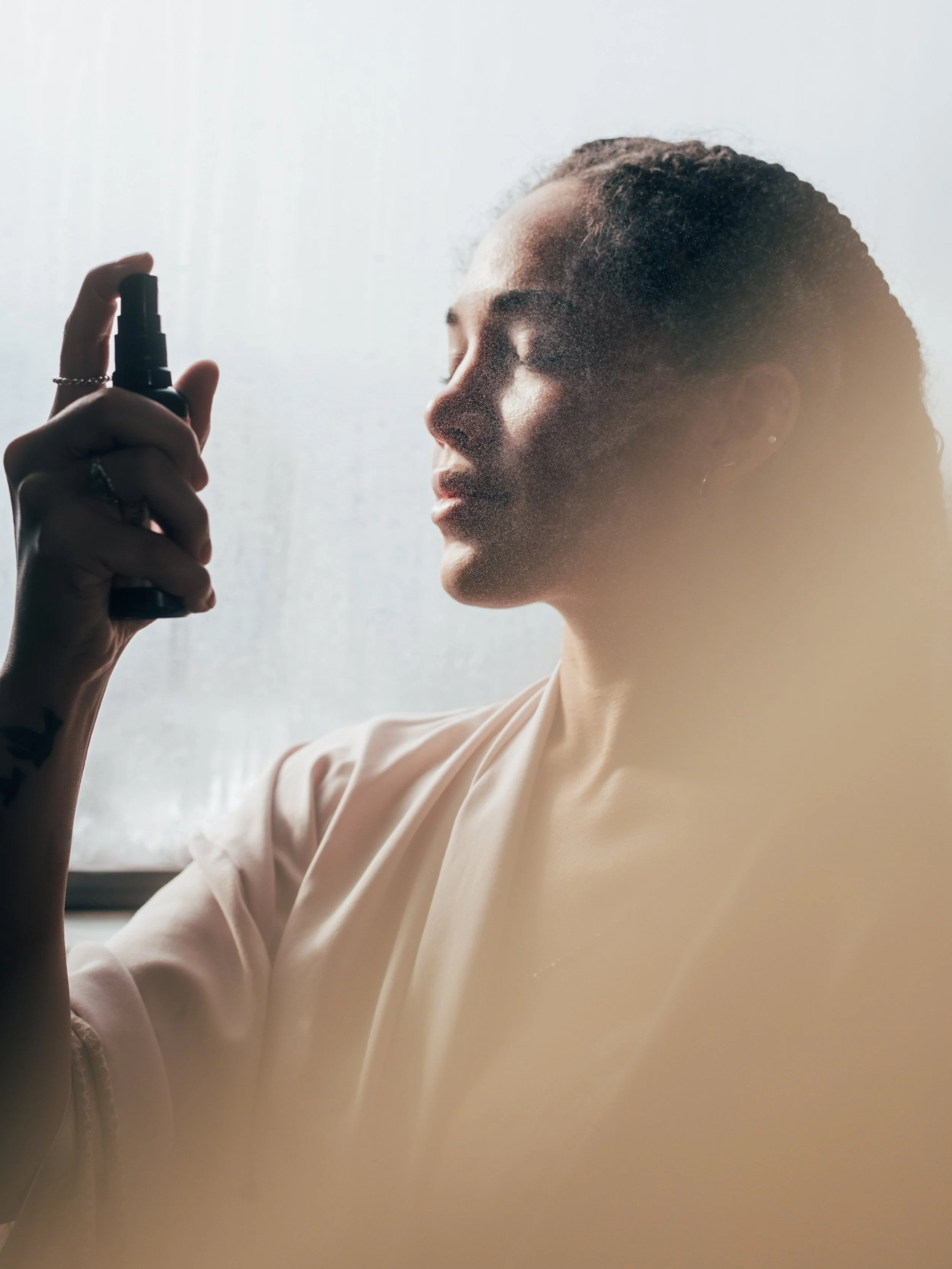 Woman spraying mist on face with closed eyes