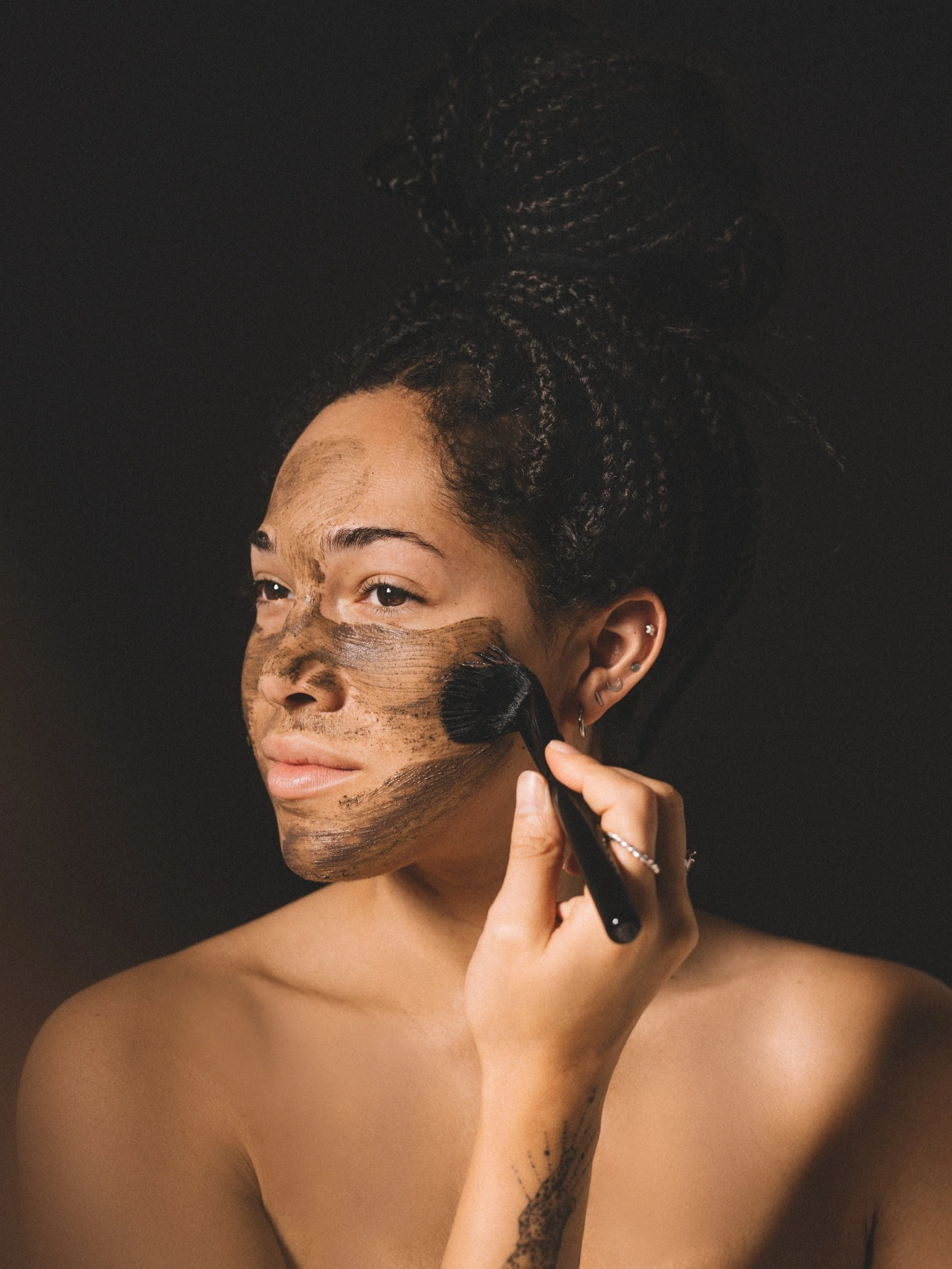 Person applying brown face mask with a makeup brush on dark background