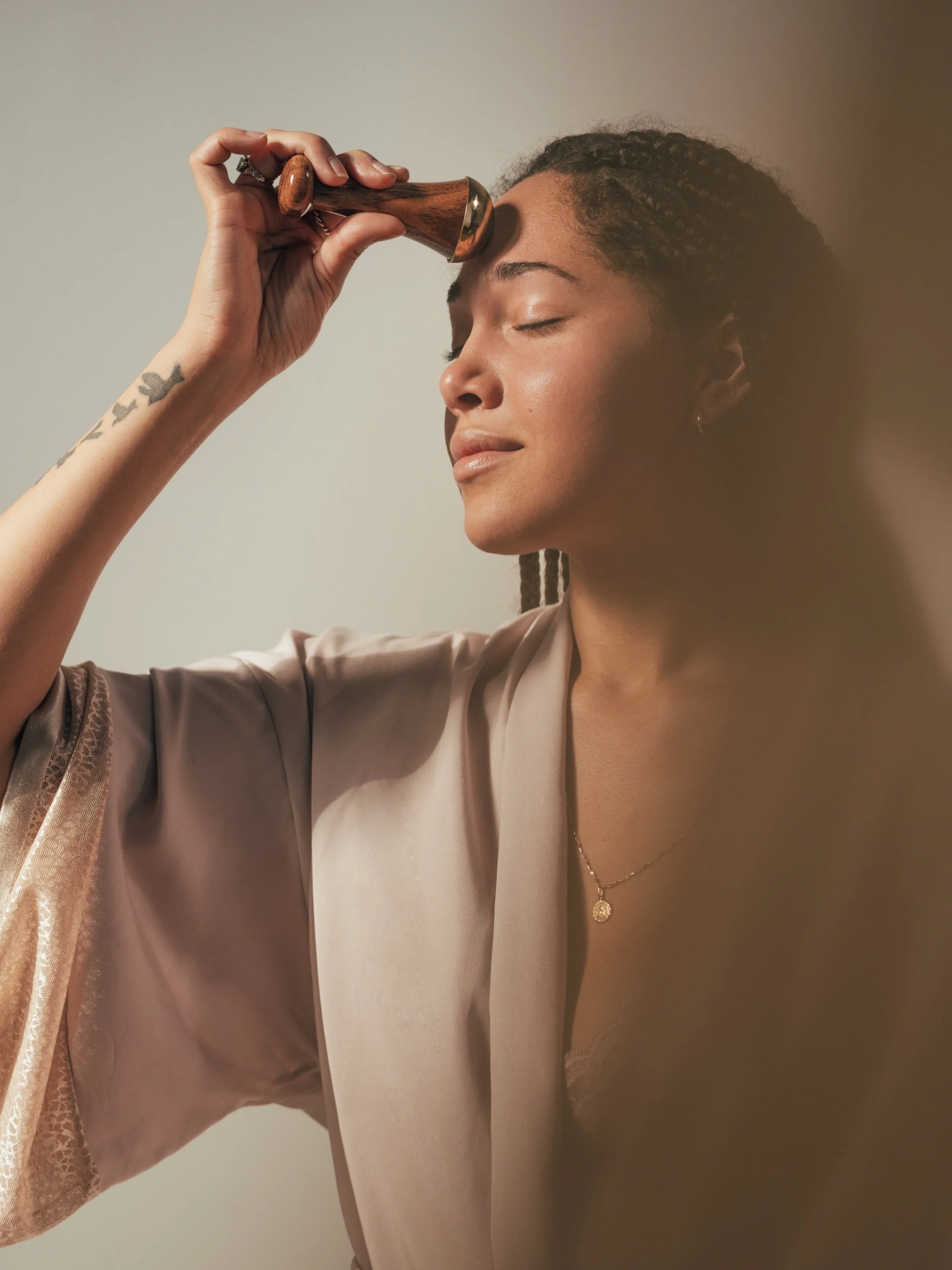 Person using a wooden face massager on forehead, wearing a robe, eyes closed.
