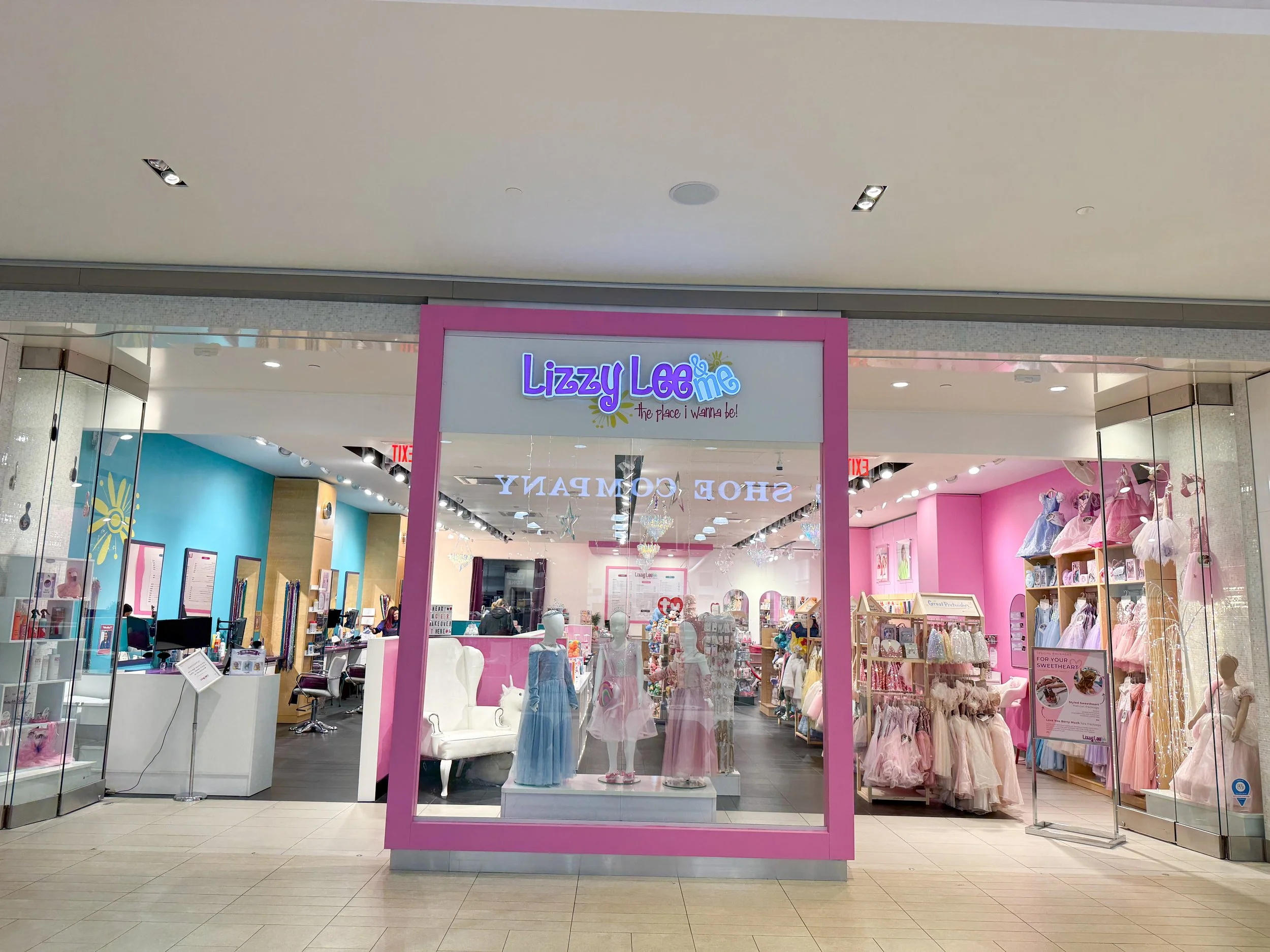 Storefront entrance for Lizzy Lee, a children's clothing shop in a shopping mall, with mannequins displaying girls' dresses and pink decor.