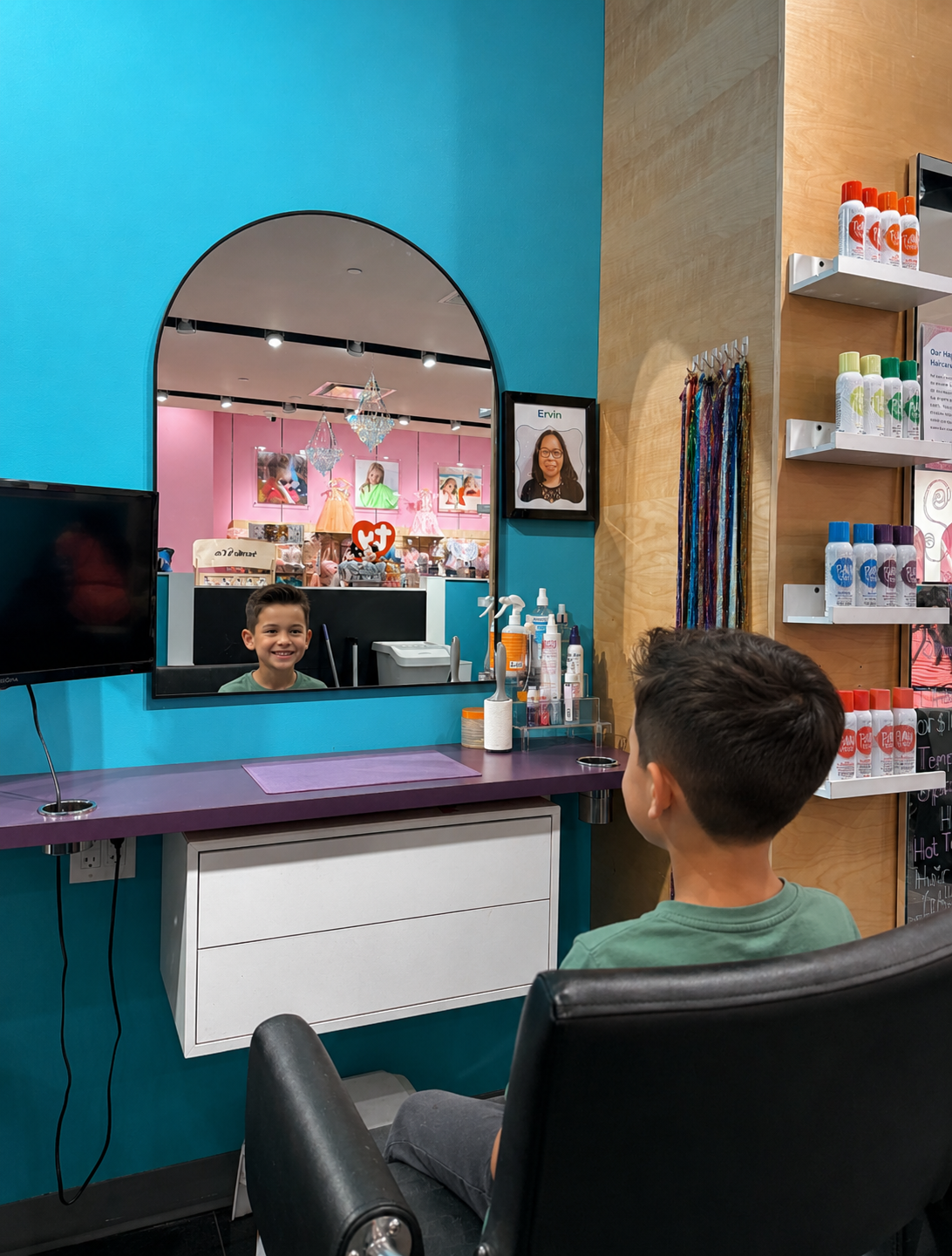 Young boy in a salon looking at his reflection in the mirror, with hair styling products on the counter and a colorful boutique visible through the mirror's arch-shaped window.