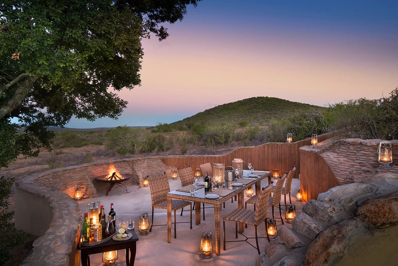 Outdoor dining area with a table, chairs, and lanterns, overlooking a scenic landscape at dusk.