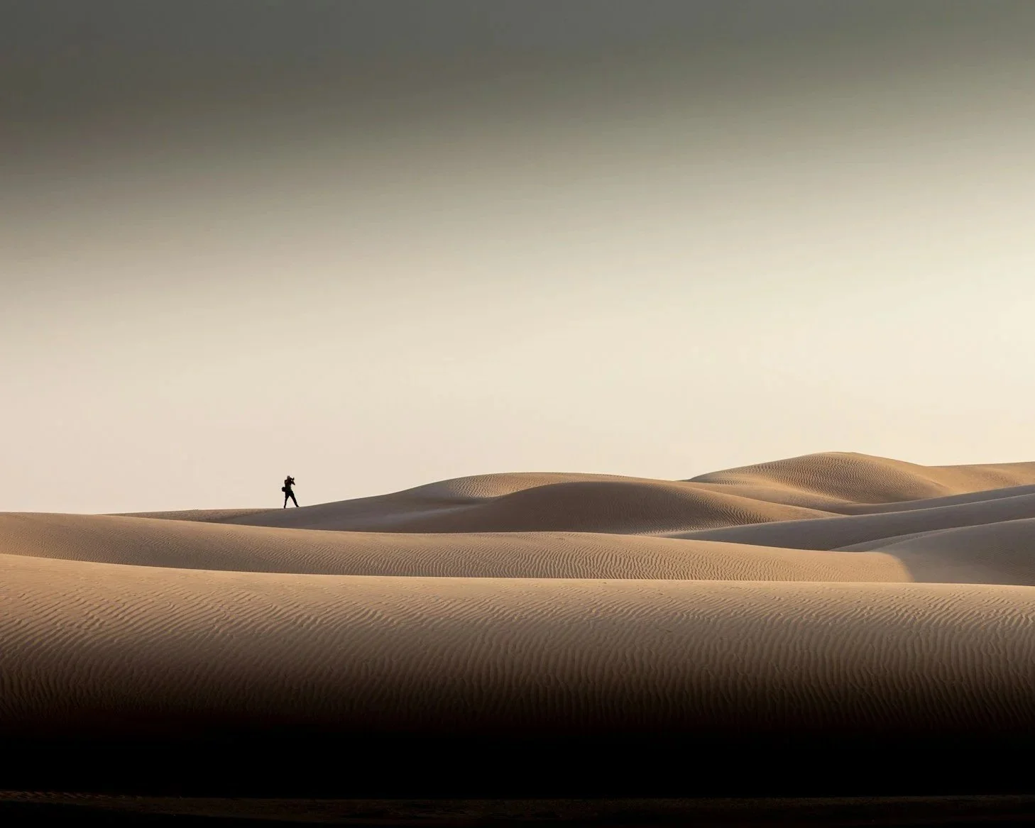 A person walking on sand dunes in a desert during sunset or sunrise.