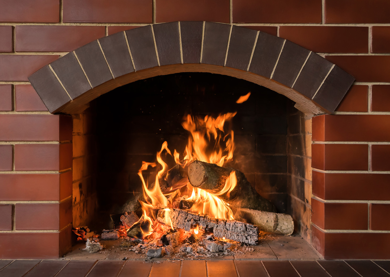 A fireplace with burning logs and visible flames inside a brick mantel.