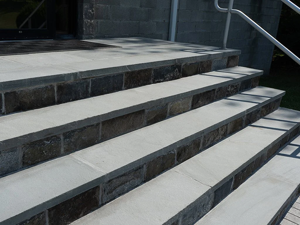 Stone stairs leading to a door with a metal railing on the side.