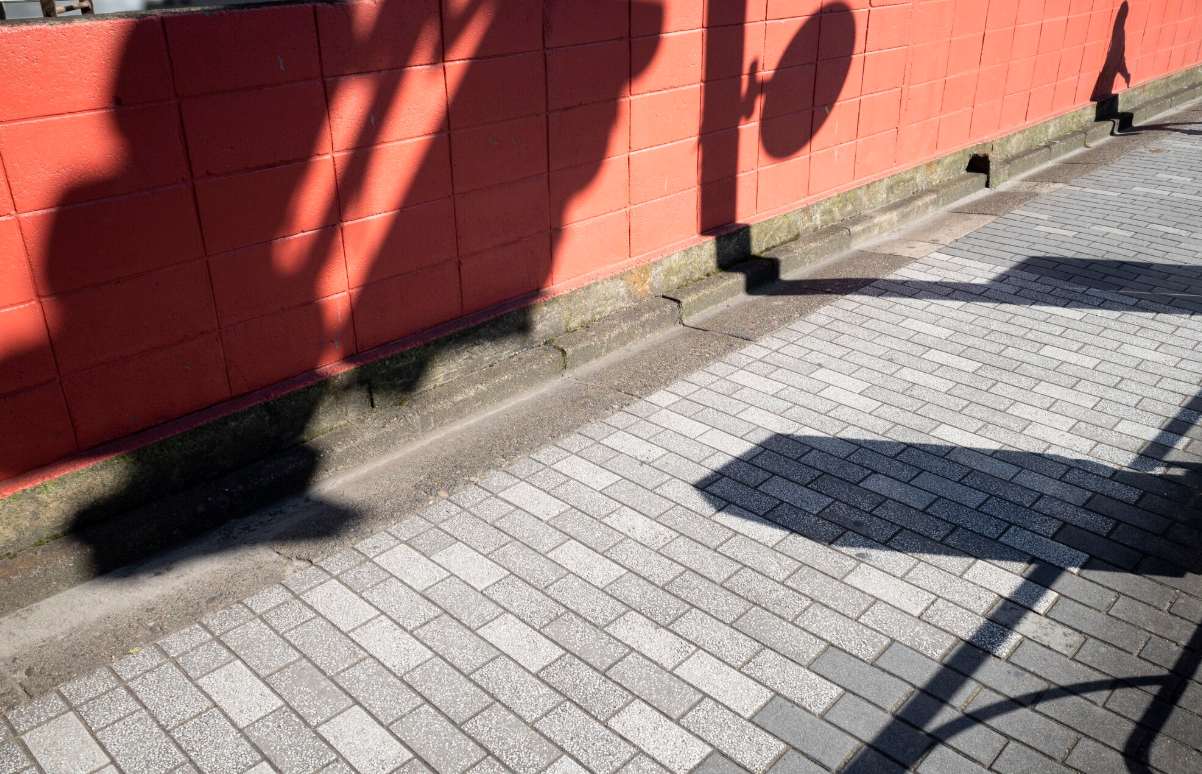 Shadows of hanging flower baskets cast on a red brick wall and paved sidewalk.