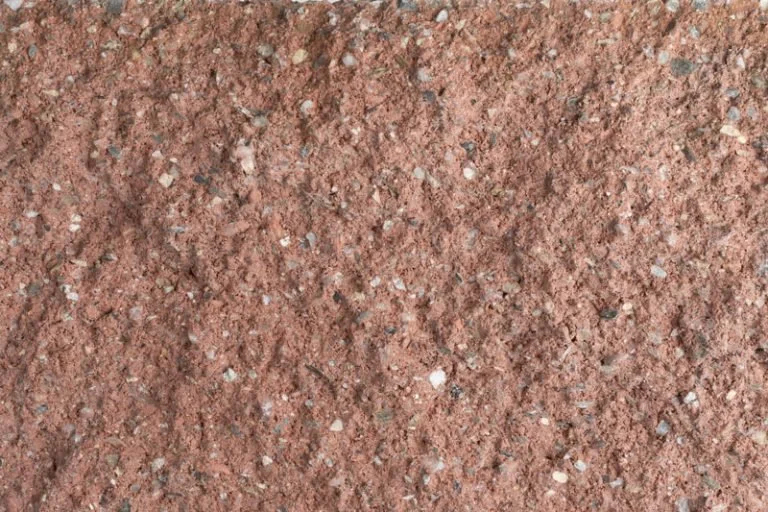 Close-up of a rough, red gravel surface with small white and gray stones.