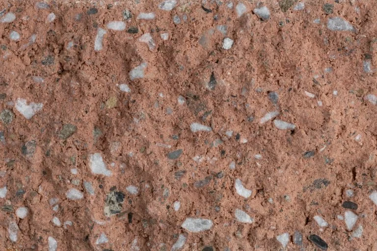Close-up of red soil with small white, black, and gray pebbles embedded in it.