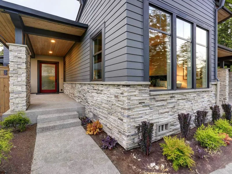 Front entrance of a modern house with stone and gray siding, large windows, and landscaped garden.