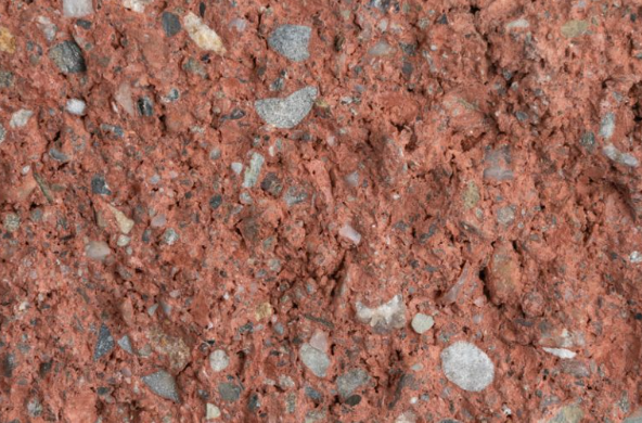 Close-up of a red, gravelly dirt surface with small stones and pebbles embedded.