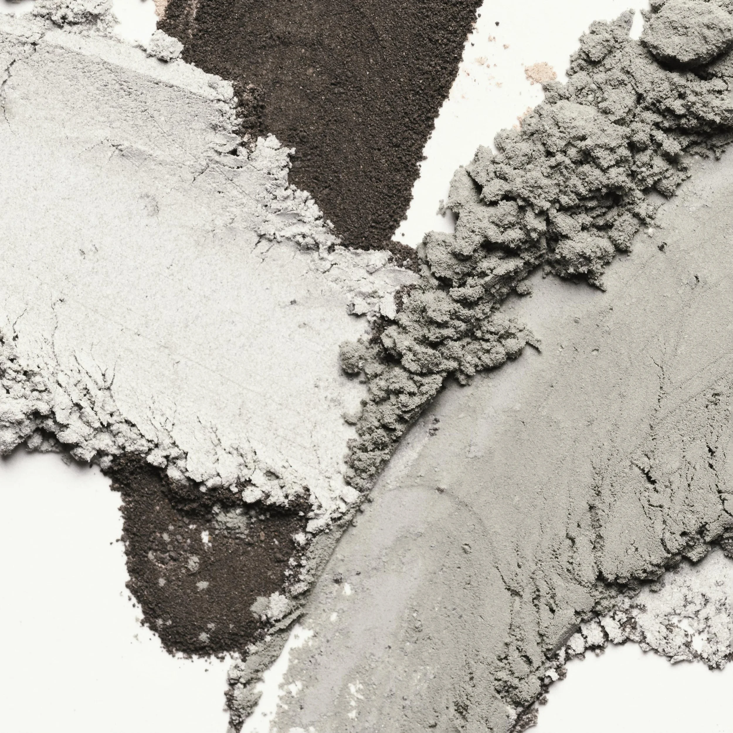 Close-up of various powdered substances in gray, black, and white colors, scattered on a flat surface.