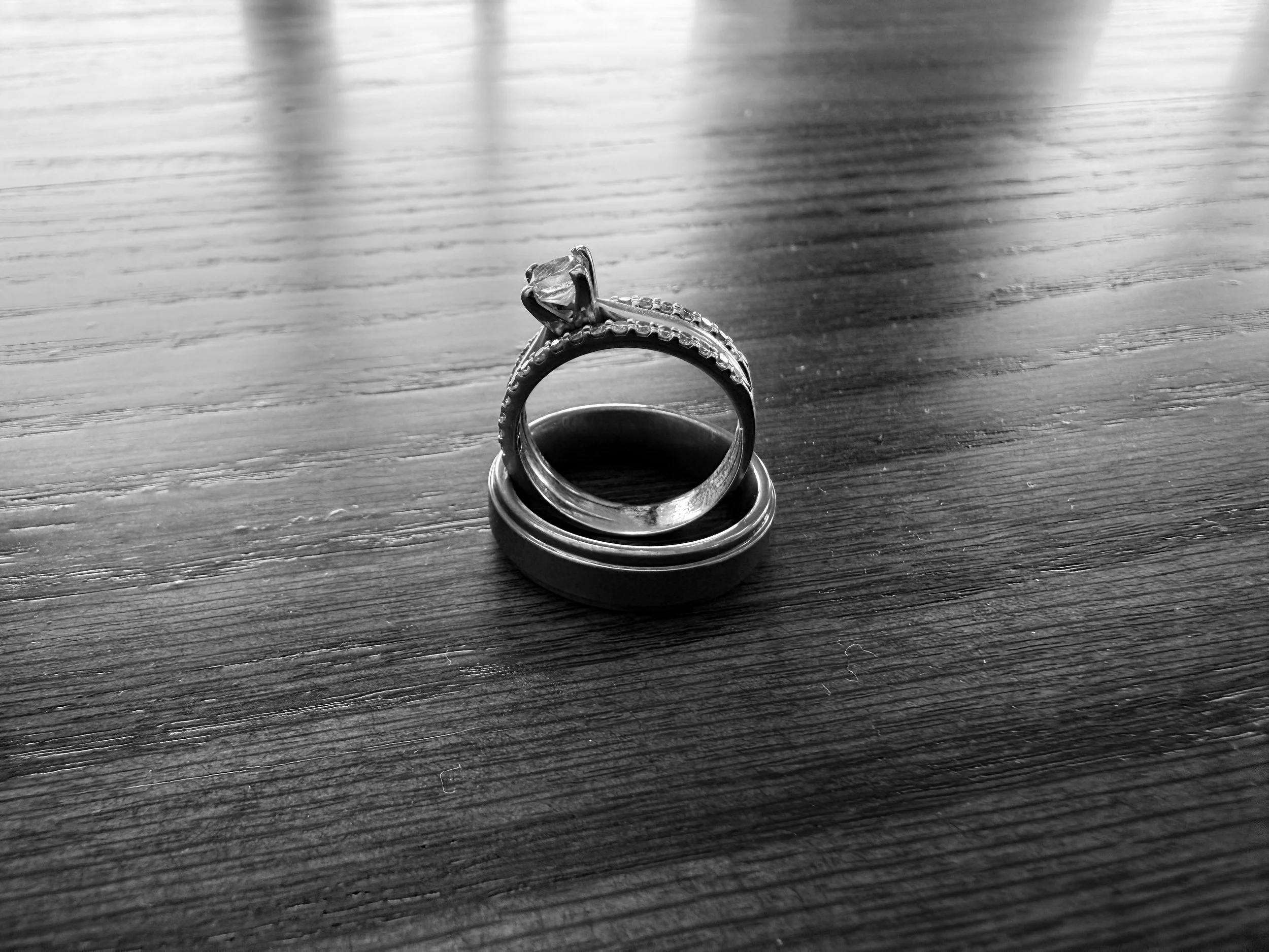 A silver ring with a large central gemstone on a wooden surface, with several wedding bands stacked underneath.