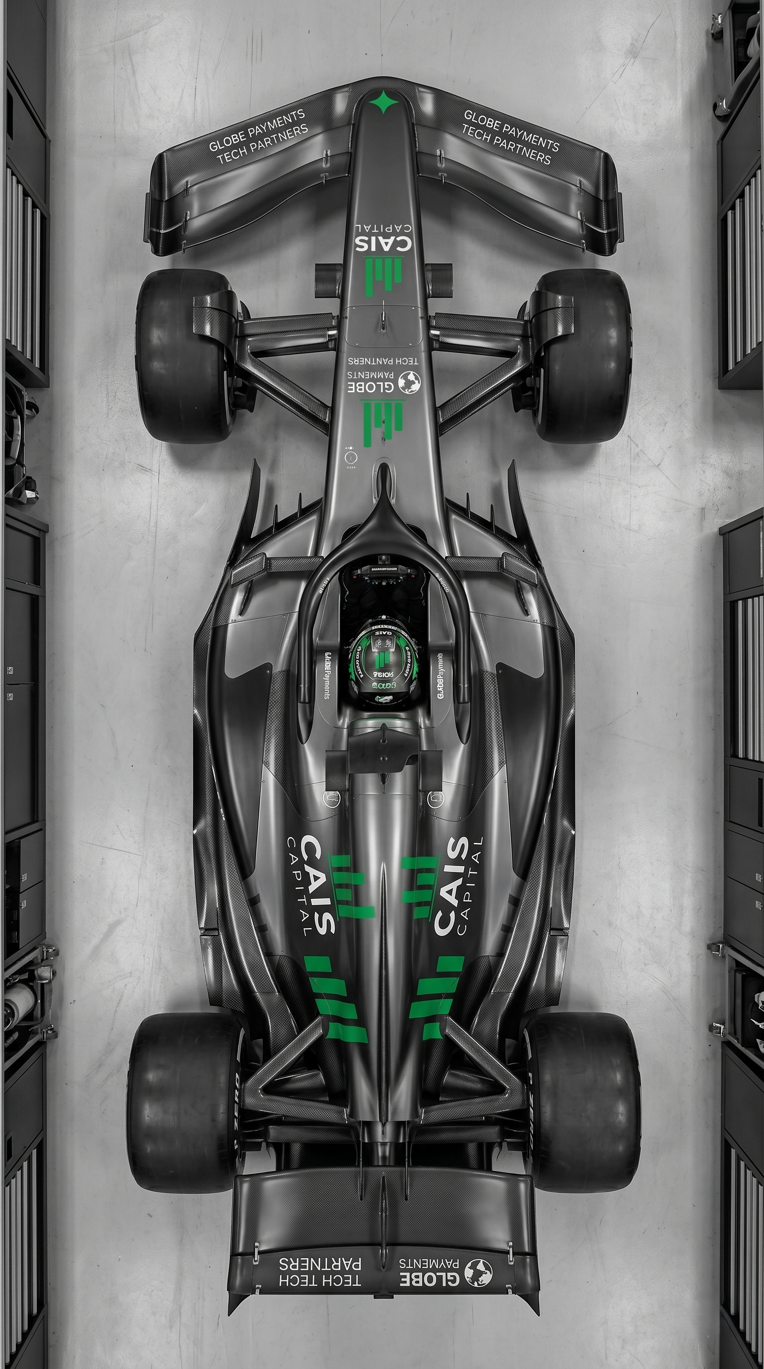 Top-down view of a sleek, black racing car with green and white sponsorship logos, parked in a garage.