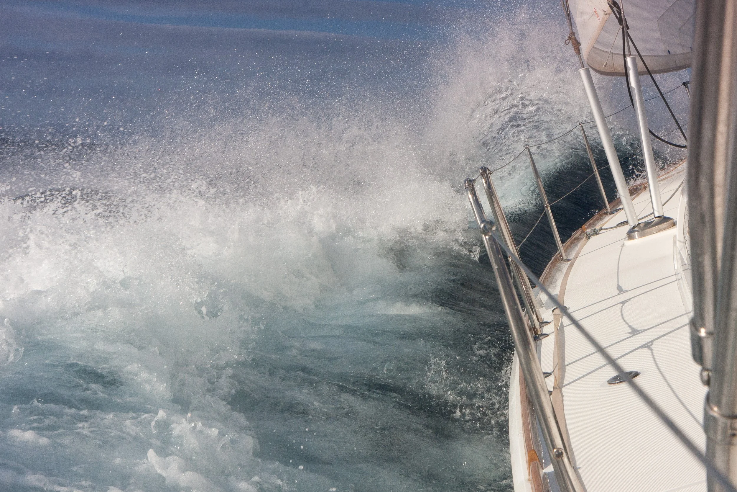 A boat moving through the water creates a large wake and spray, with a section of the boat's side and rigging visible
