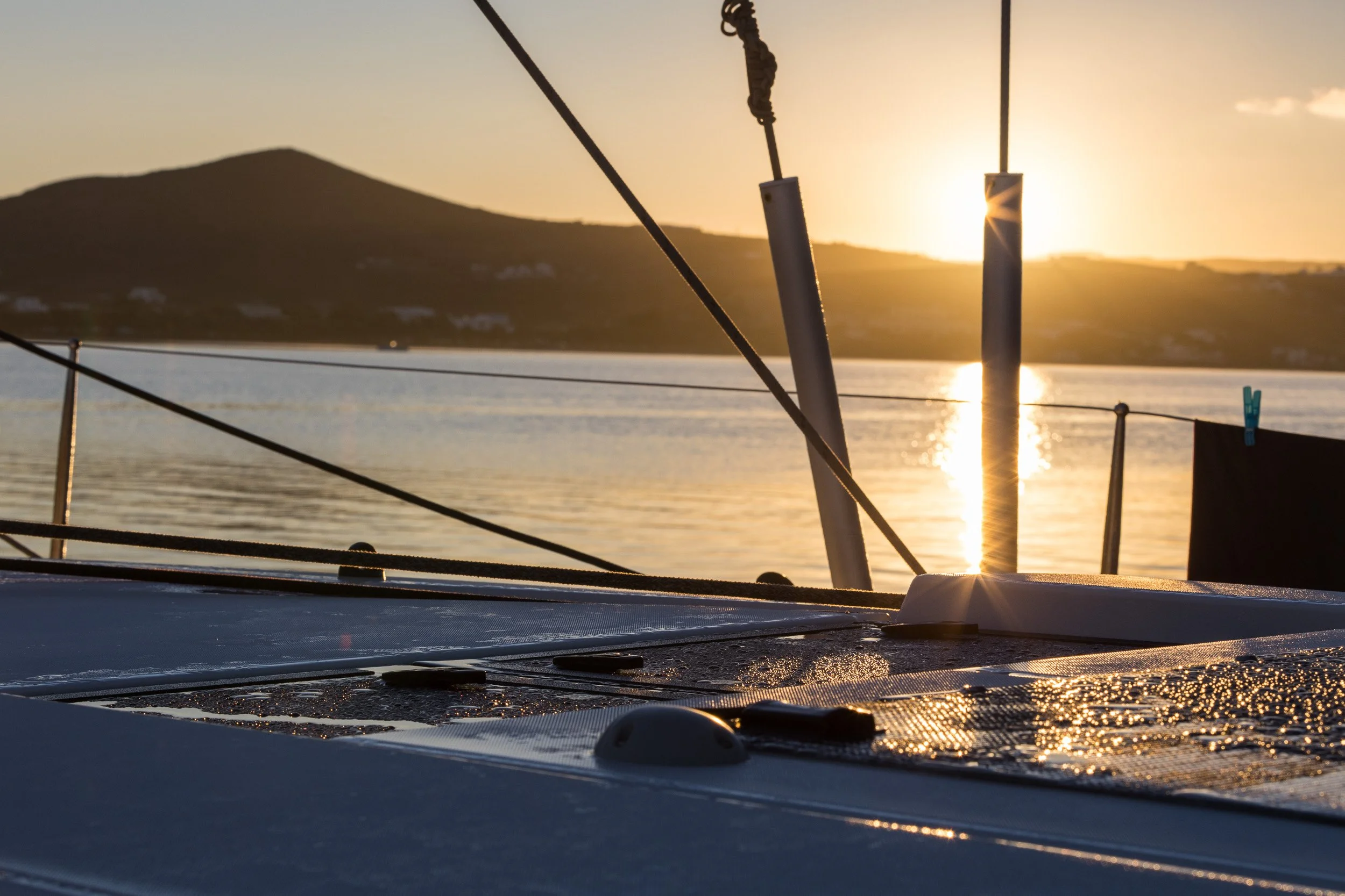 Sunset over a body of water viewed from a boat, with ropes and boat fittings in the foreground.