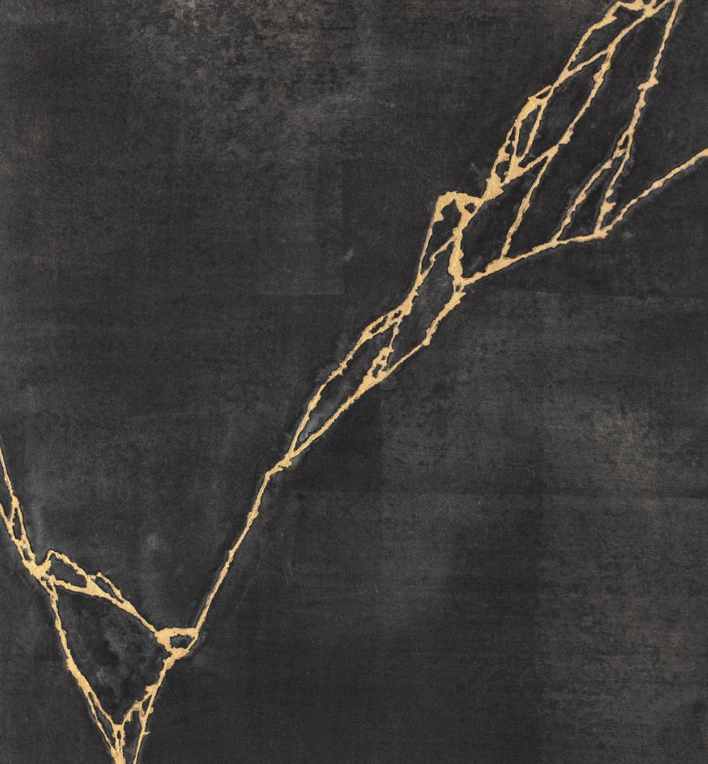 Close-up of black surface with gold-colored textured lines forming an abstract shape.