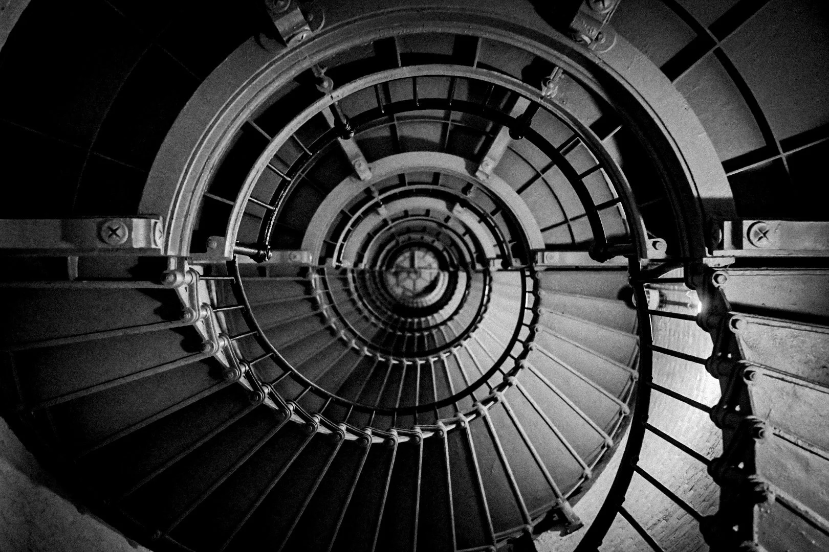 Looking down a spiral staircase with metal railings and steps, captured from the top in black and white.
