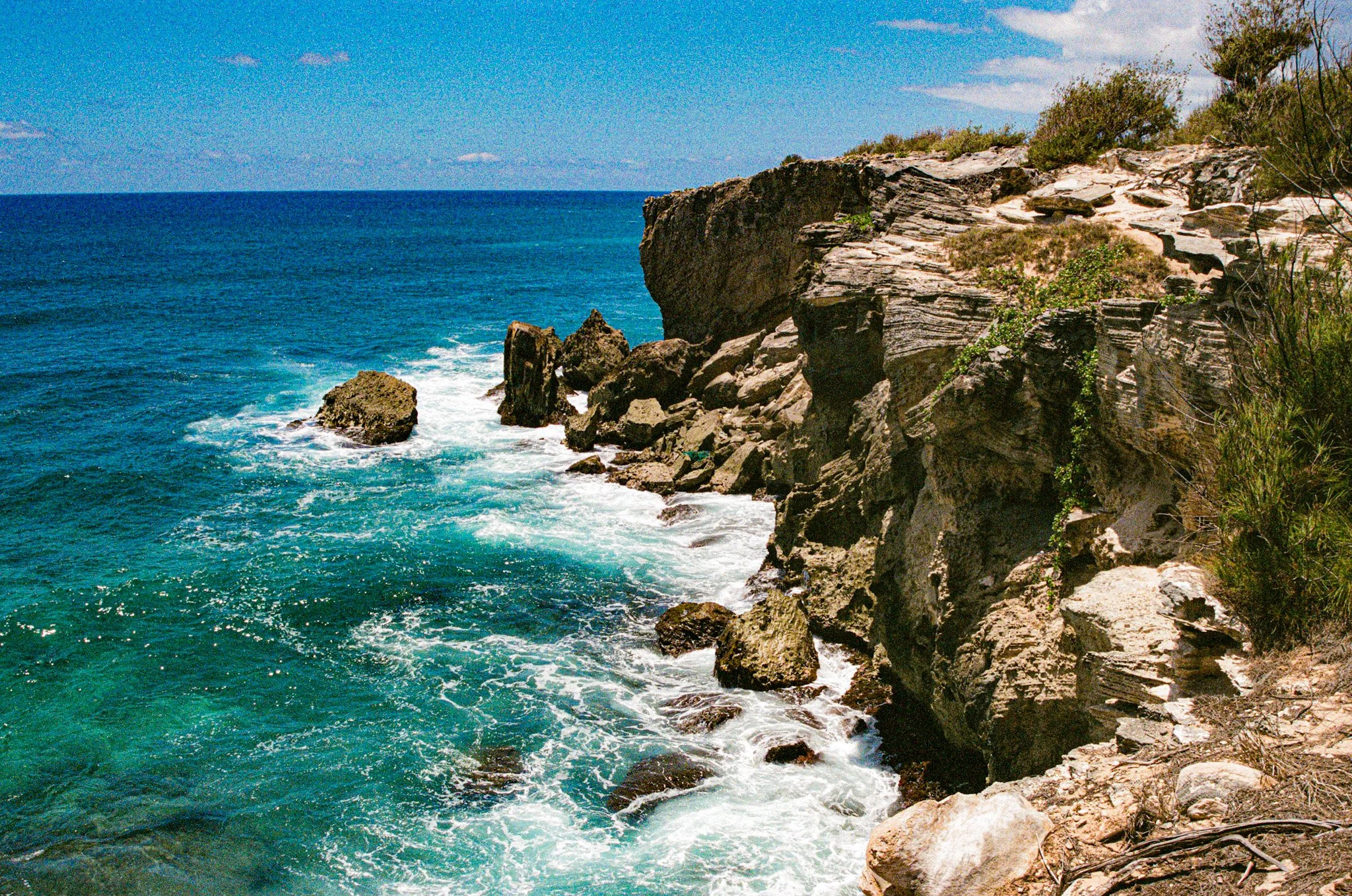 Cliffside overlooking the ocean with rocks and sparse vegetation under a blue sky