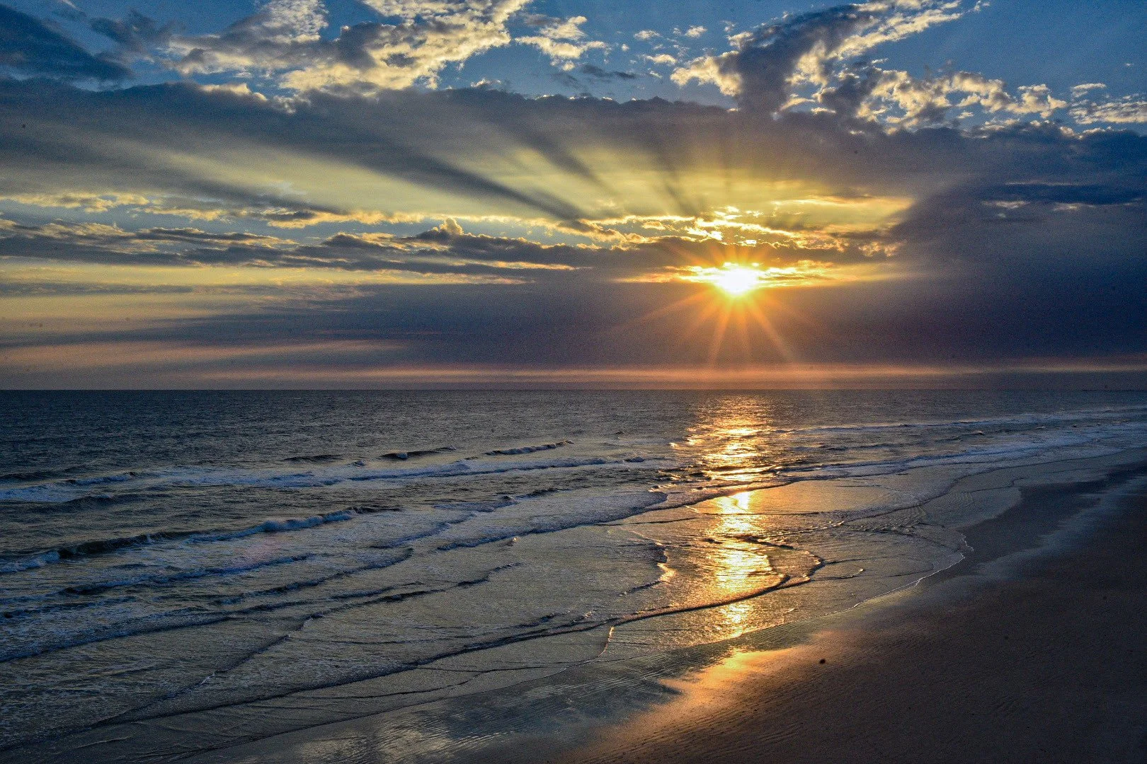 Sunset over the ocean with clouds and gentle waves on the beach.