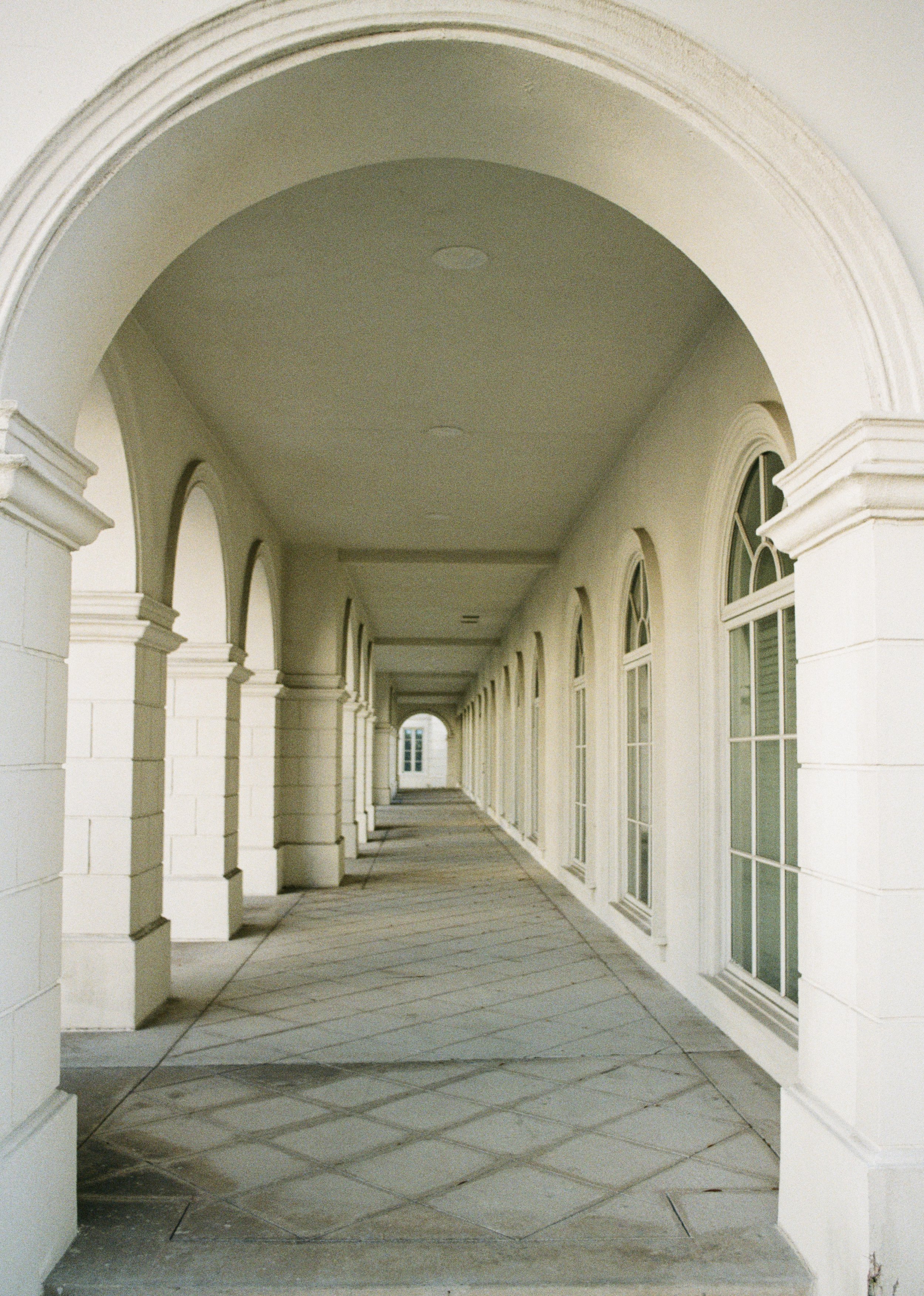 A long, covered outdoor walkway with arched ceilings and large windows on the side.