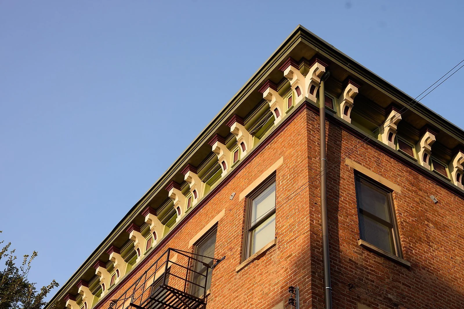 Corner of a brick building with decorative window trim and a small balcony, under a clear blue sky.
