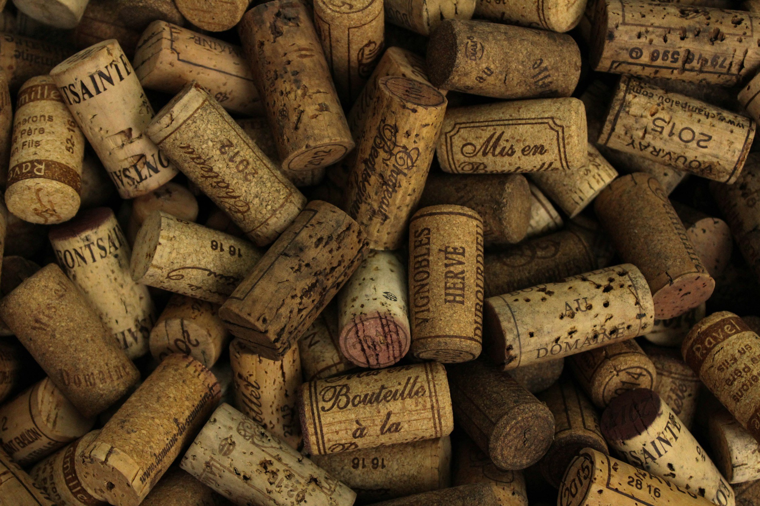 Close-up of numerous wine corks with printed labels, showing various worn and stained corks in assorted shades of tan and brown.