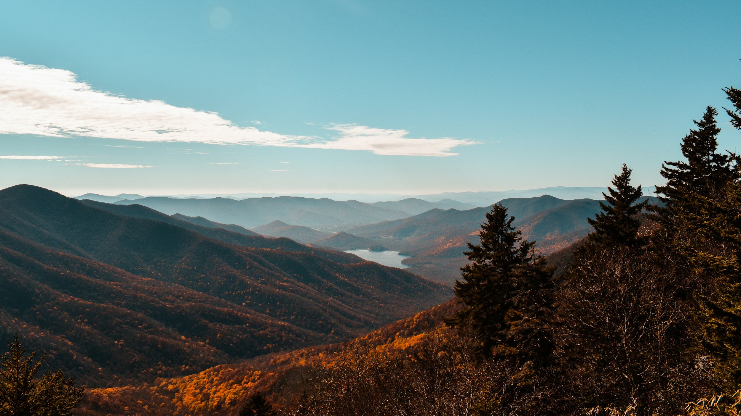 Scenic view of mountain range with hills, a river, and trees, under a partly cloudy sky