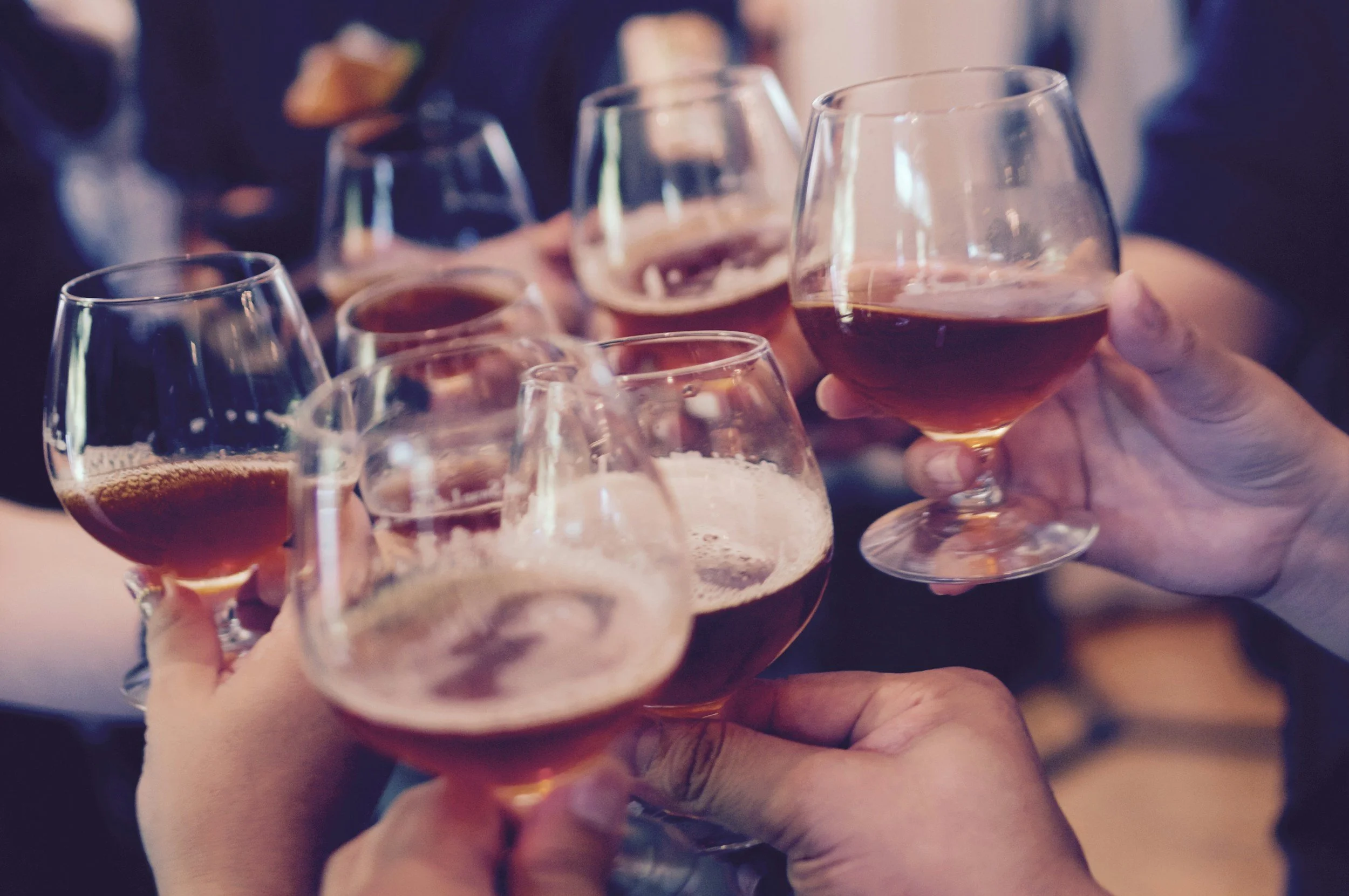 People clinking glasses filled with dark beer or ale in a toast at a social gathering.