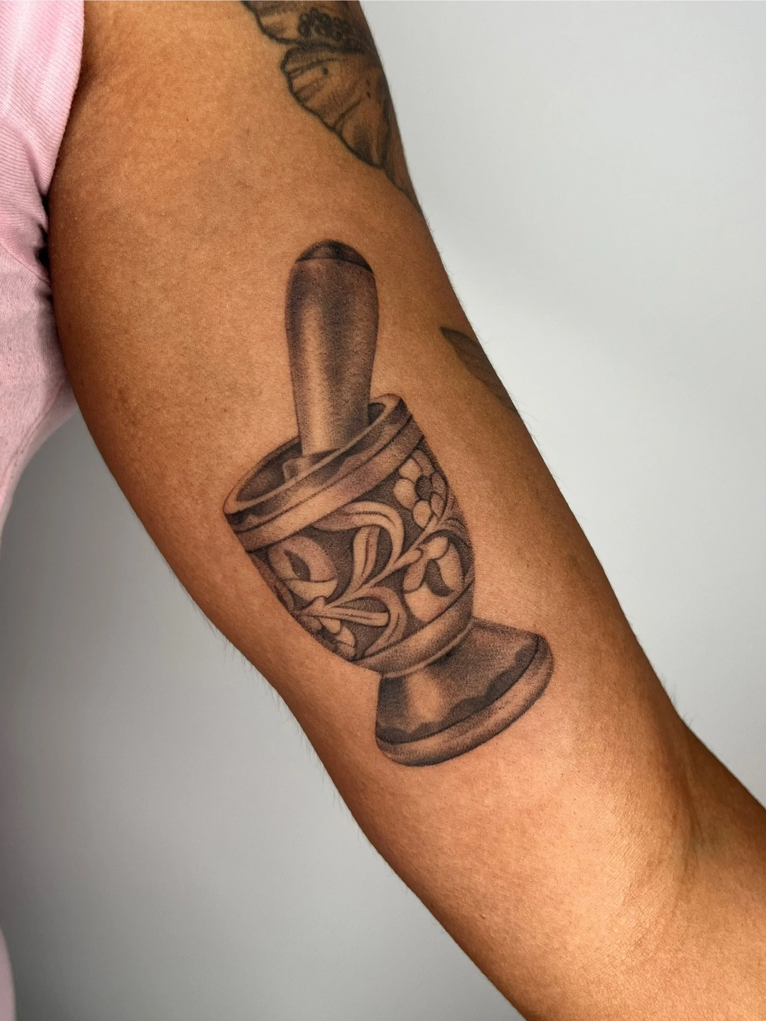 Close-up of a person's upper arm showing a tattoo of a mortar and pestle 