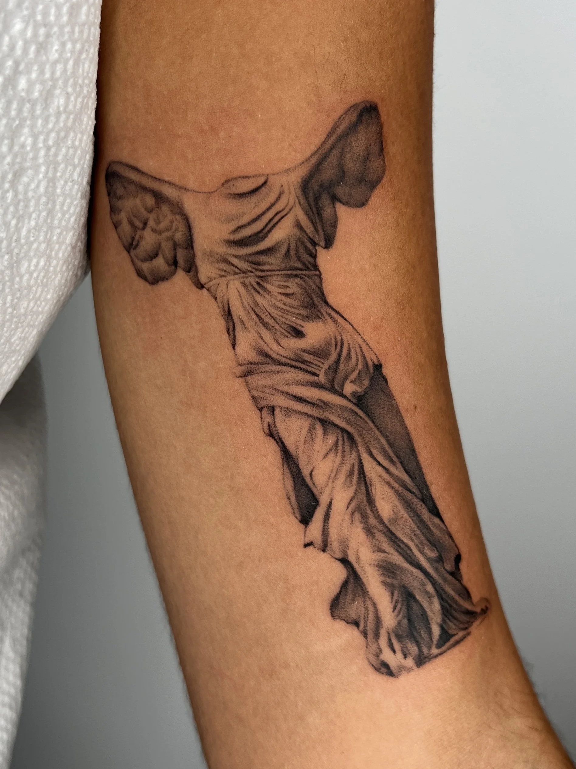 A tattoo of a winged victory statue on a person's arm