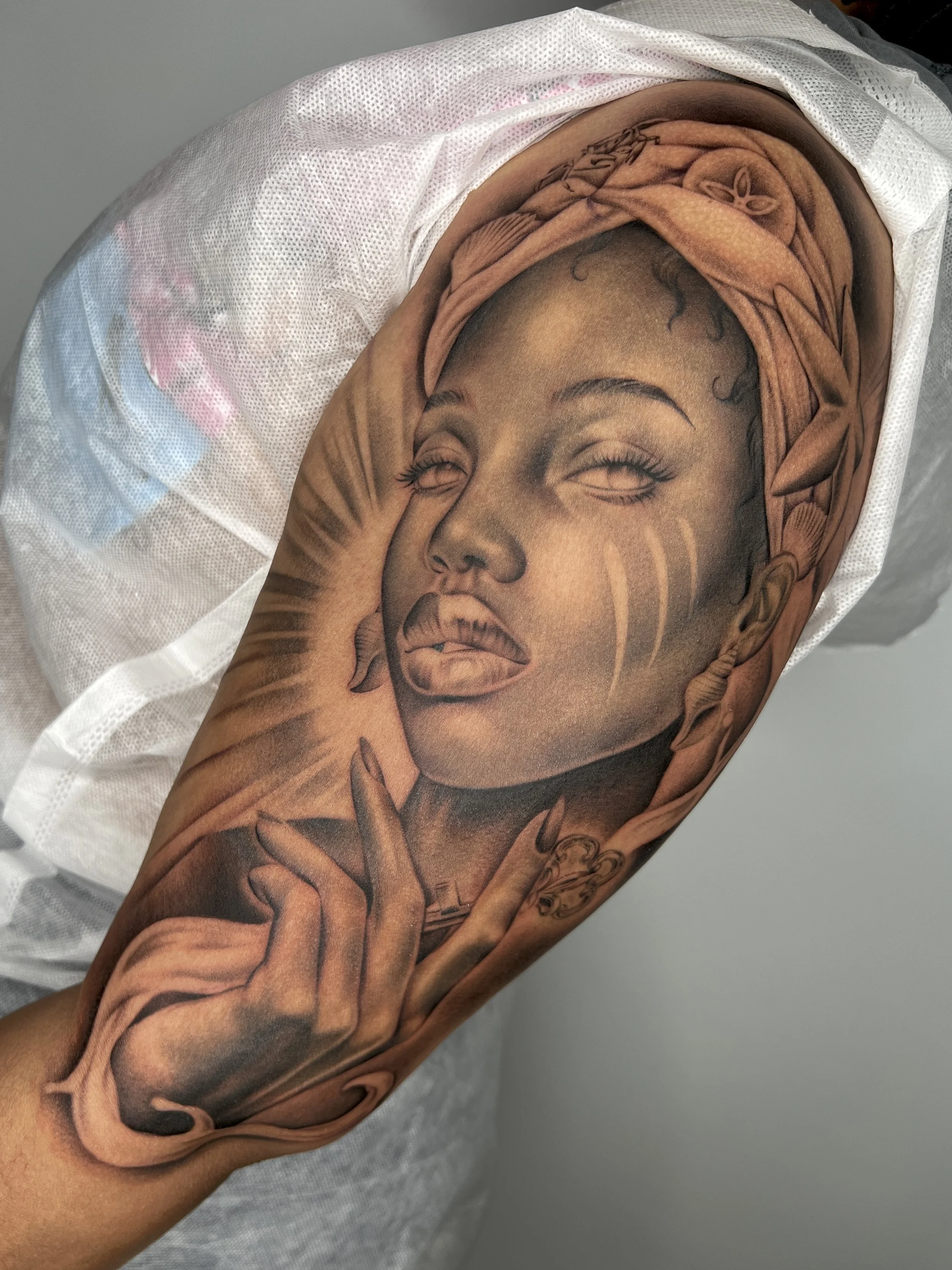 Close-up of a person's upper arm with a detailed black and gray portrait tattoo of a woman wearing a headscarf.