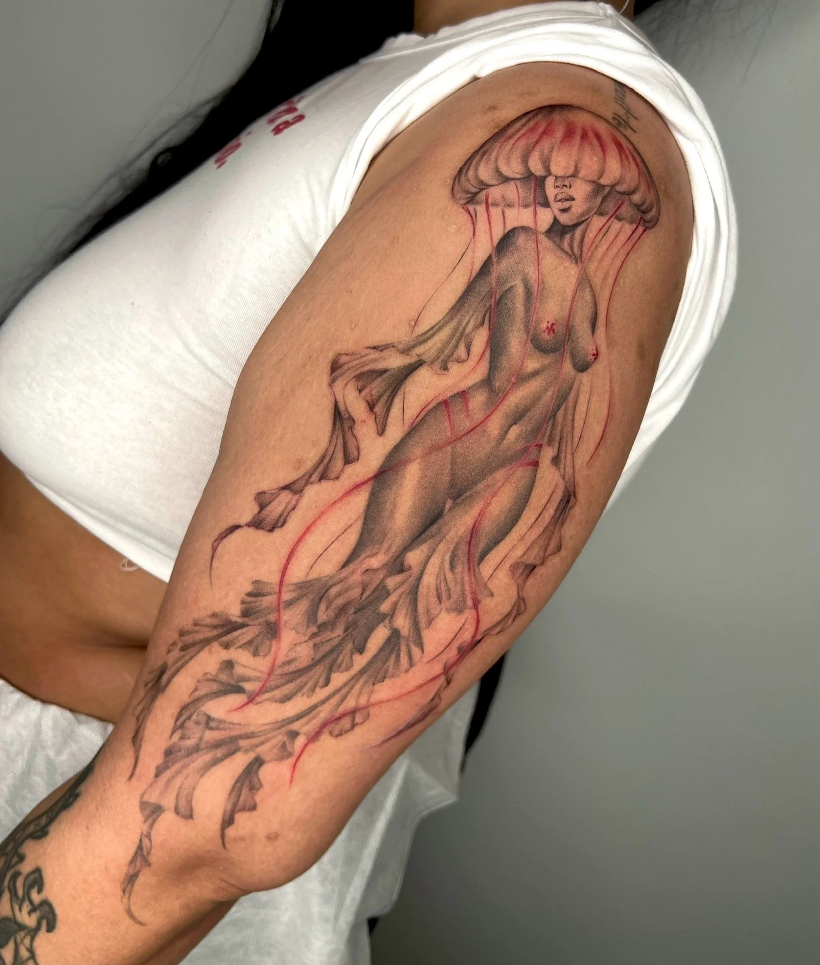 Tattoo of a realistic mermaid jellyfish woman on the upper arm.